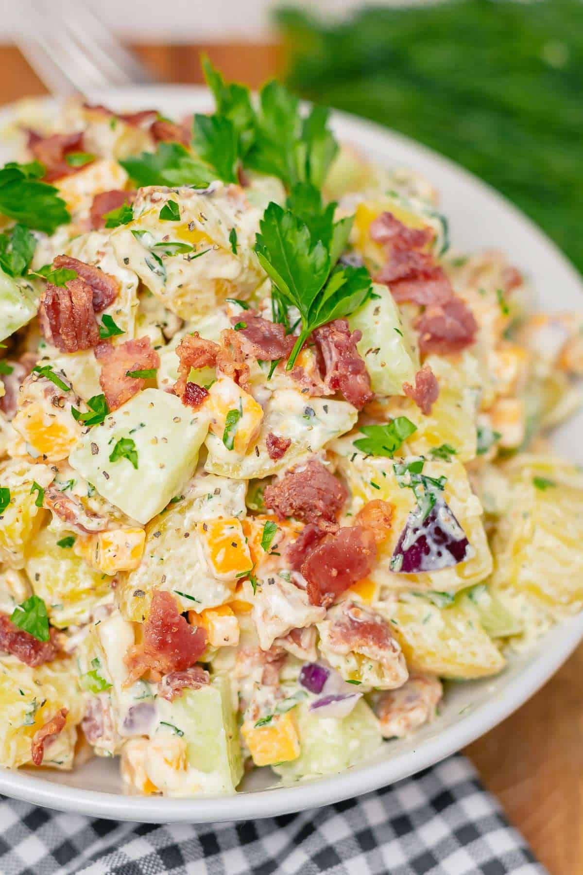 creamy potato salad with cheddar bacon cucumber in ranch dressing in a white bowl