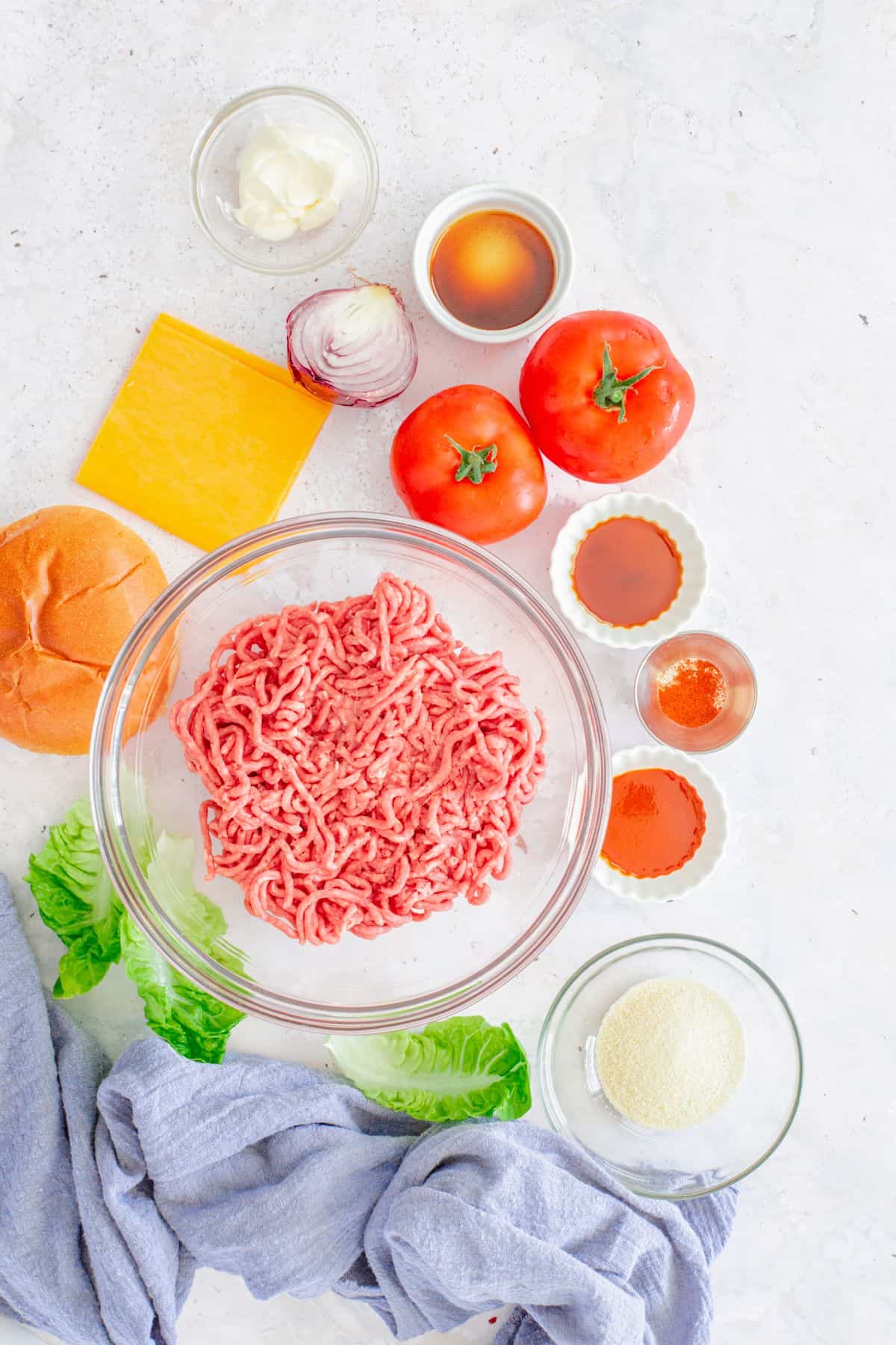 Raw ground beef with burger ingredients: cheese, buns, tomatoes, onion, lettuce, and spices