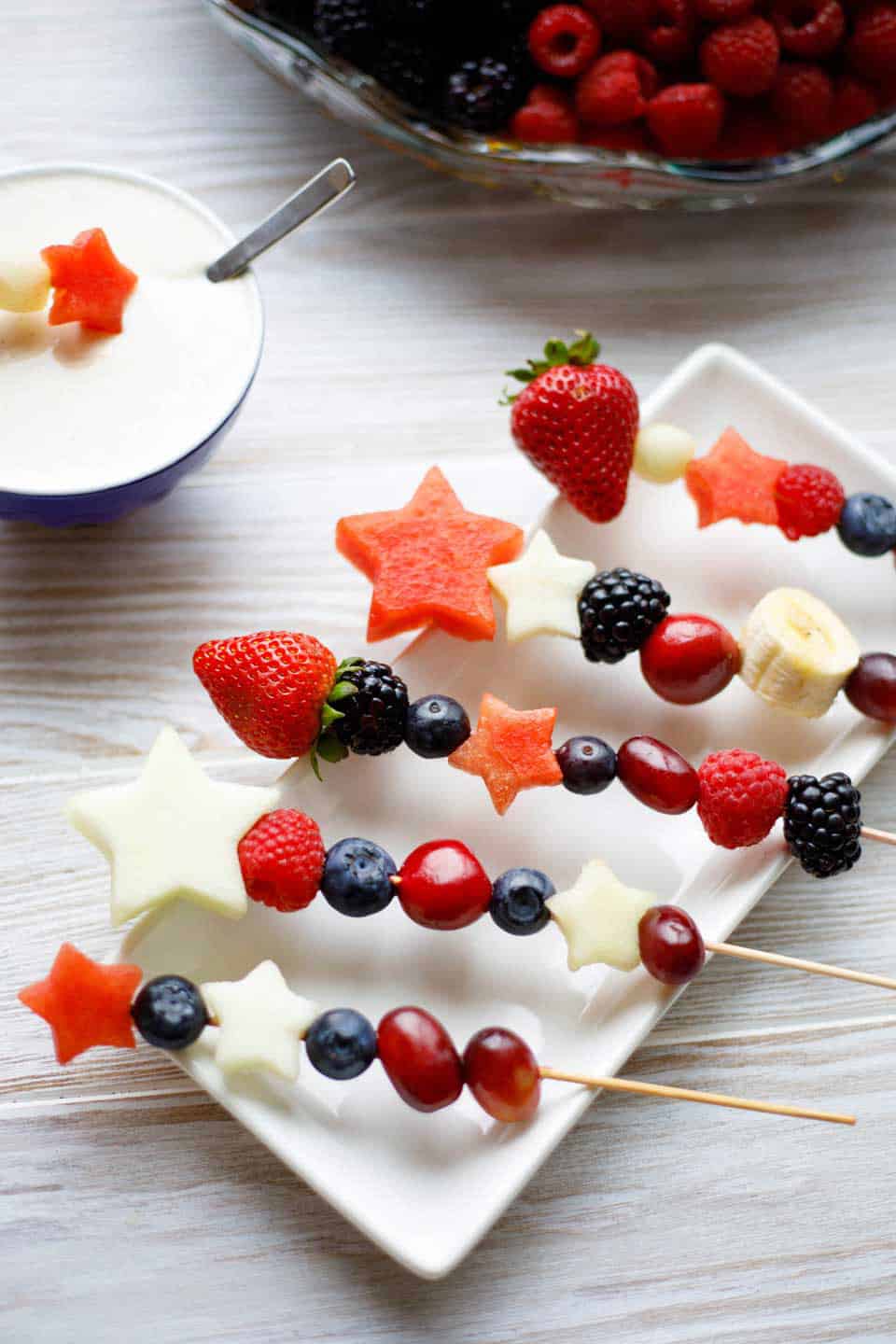 red, white and blue fruit kabobs on skewers on a serving plate.