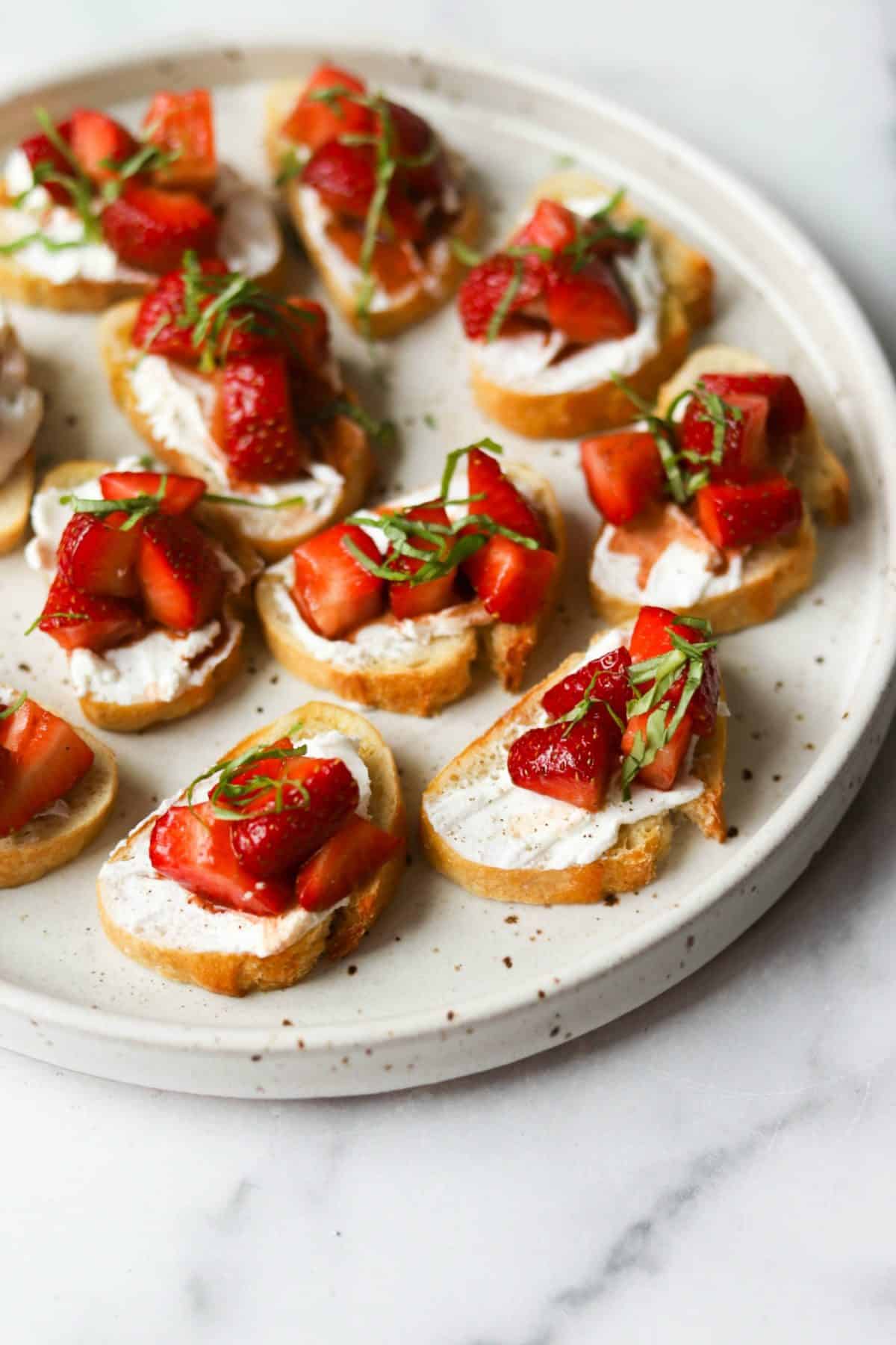 strawberry and basil bruschettas arranged on a white plate.