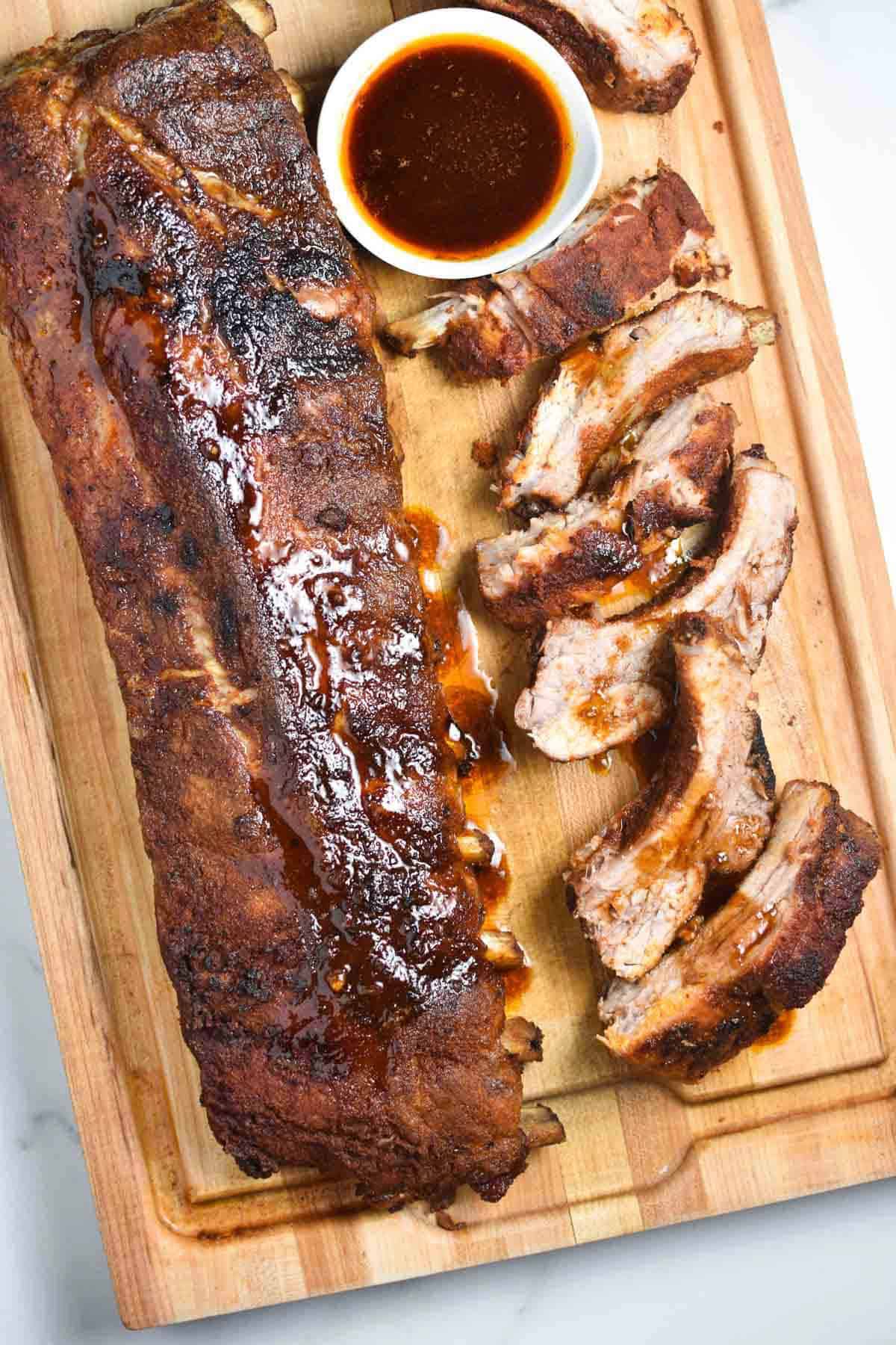 juicy bbq oven ribs rack on a wooden board with a barbecue sauce on the side.
