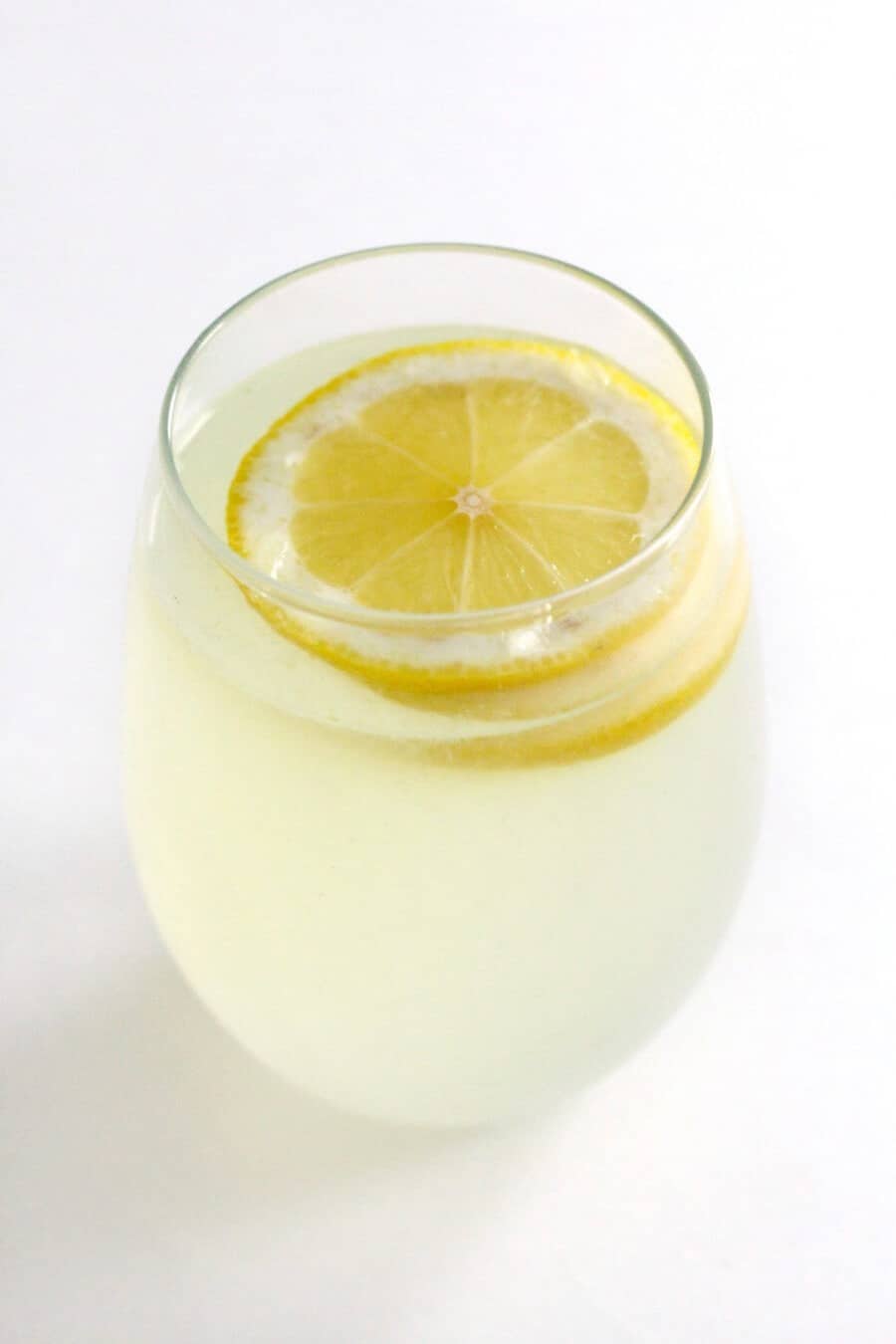 yellow lemon lemonade in a tall glass with a slice of lemon inside.