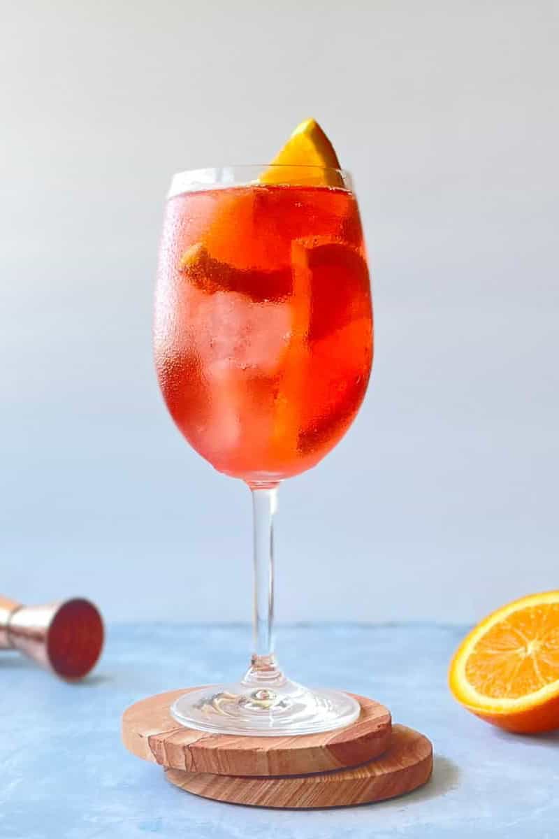red-orange colored negroni spritz cocktail in a wine glass with a slice of orange inside.