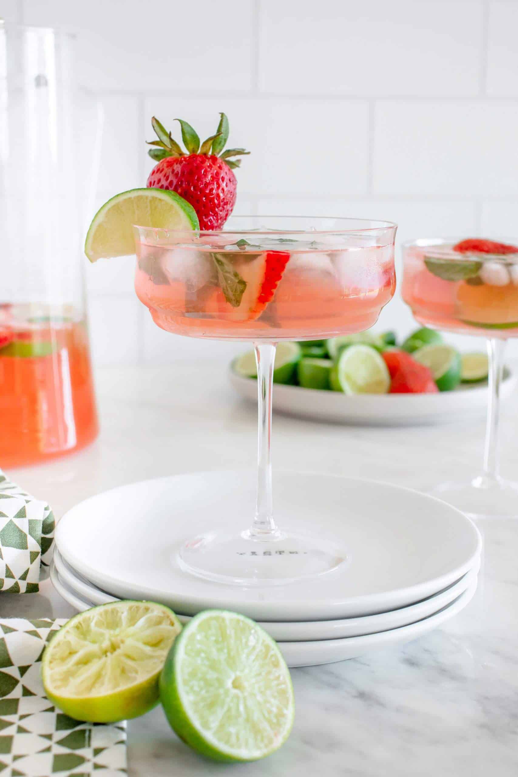 pink mojito in an old fashioned champagne glass with strawberry and lime wedge for decoration.