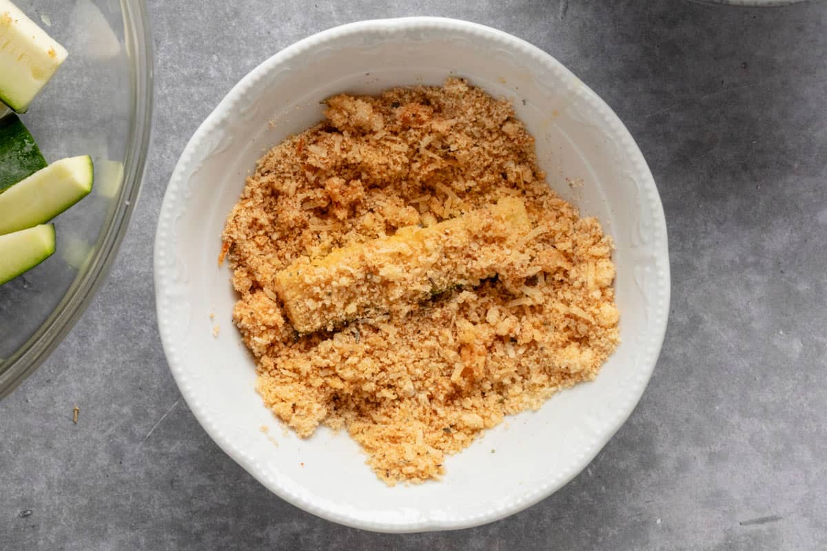 coating the zucchini sticks in almond flour and parmesan mixture.