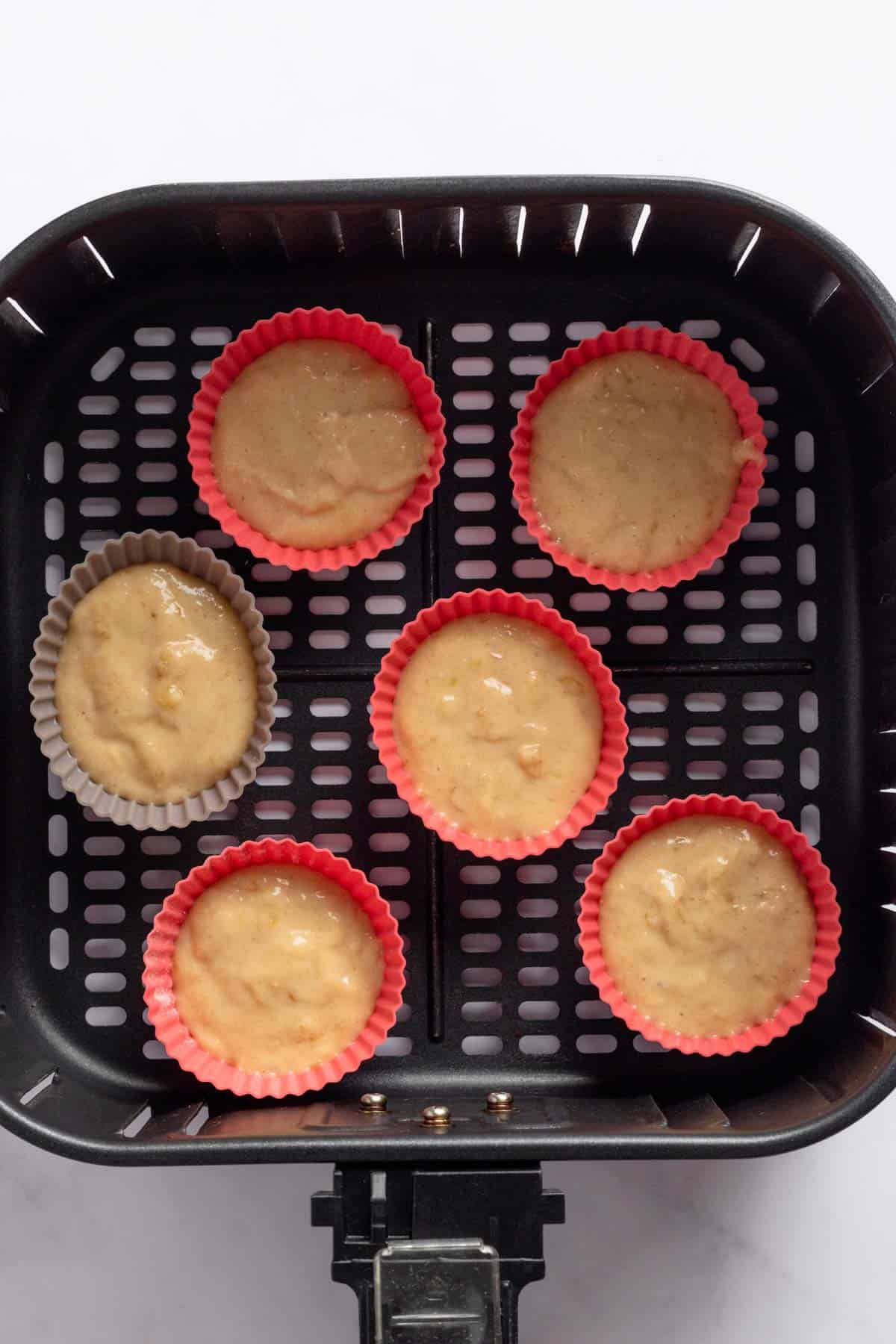 banana batter poured into silicone muffin liners in air fryer basket.