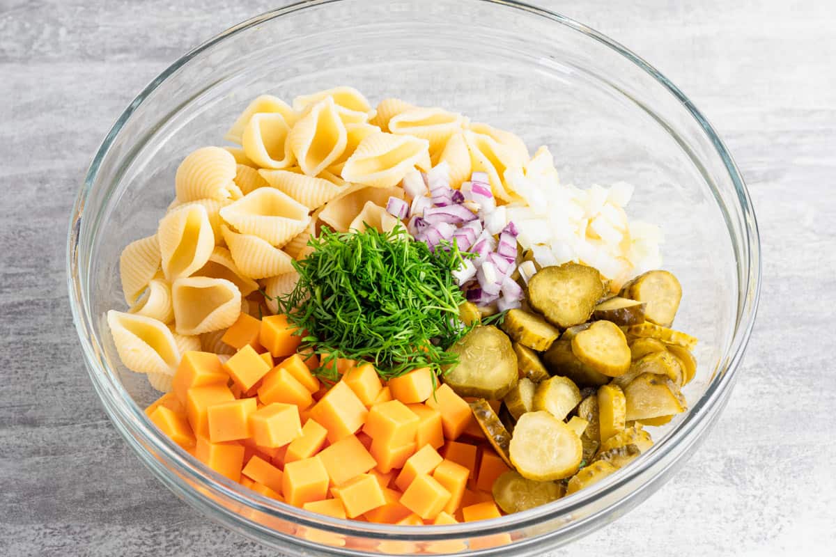shell pasta salad ingredients in a bowl with white dressing.