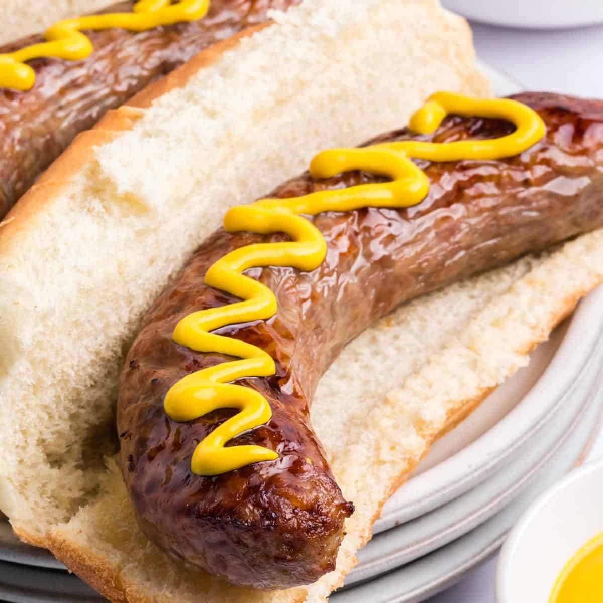 air fryer brats in buns with drizzle of mustard sauce.