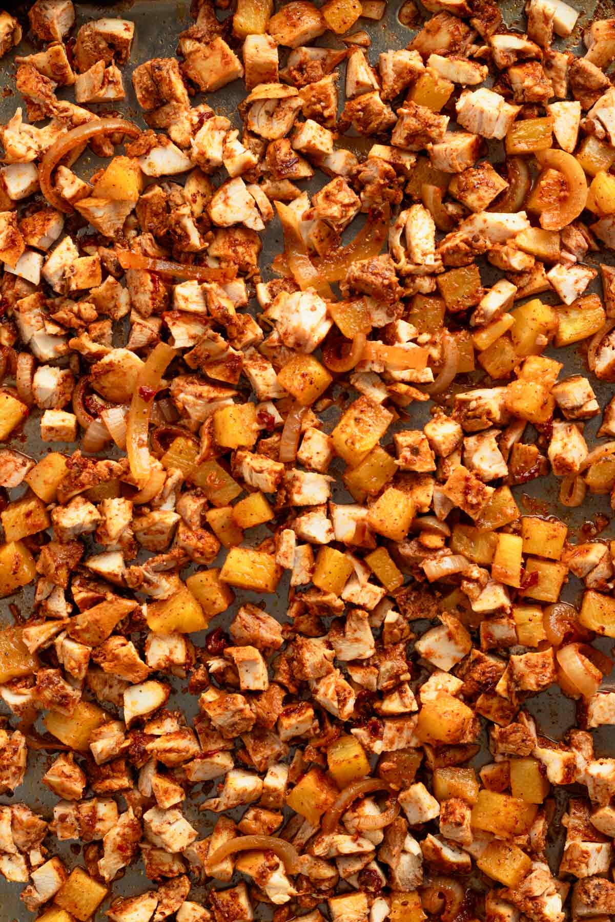 diced chicken cubes on baking pan with pineapples.