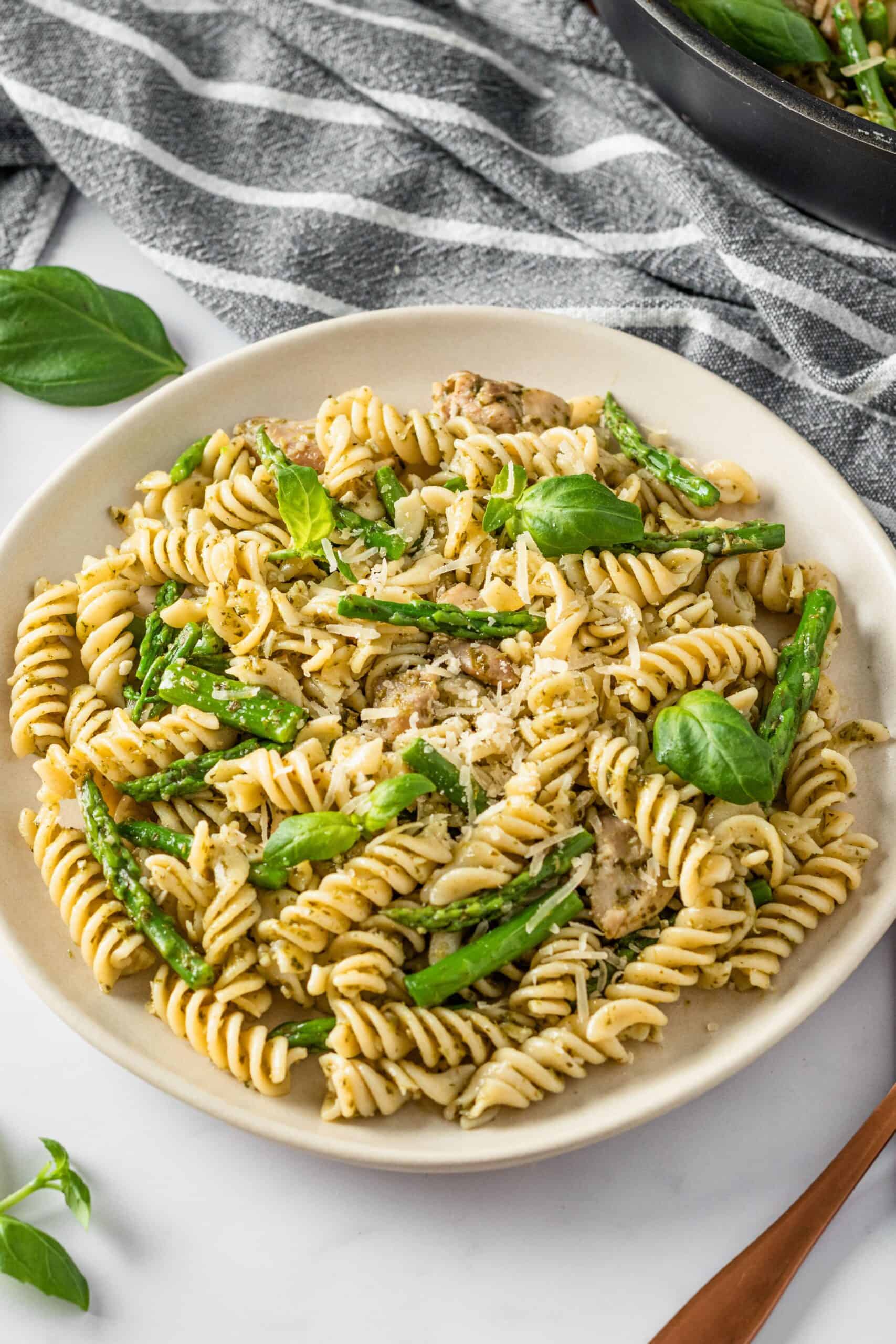 Bowl of lemon asparagus pasta with chicken, basil, and Parmesan on white table