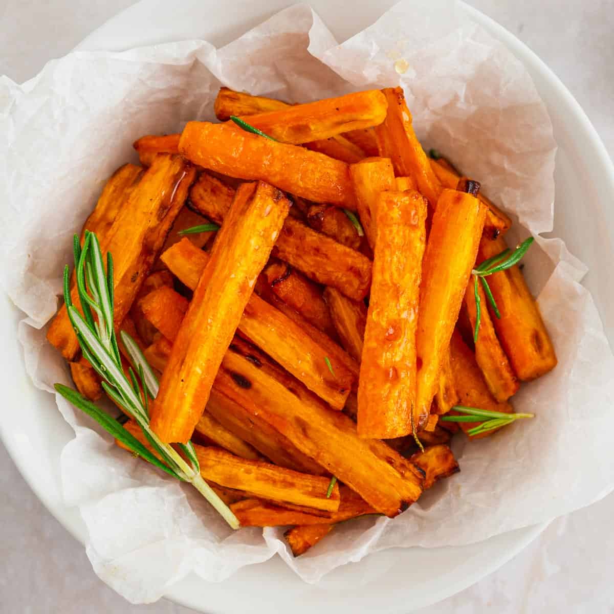 glazed carrots in a bowl with rosemary stalks.