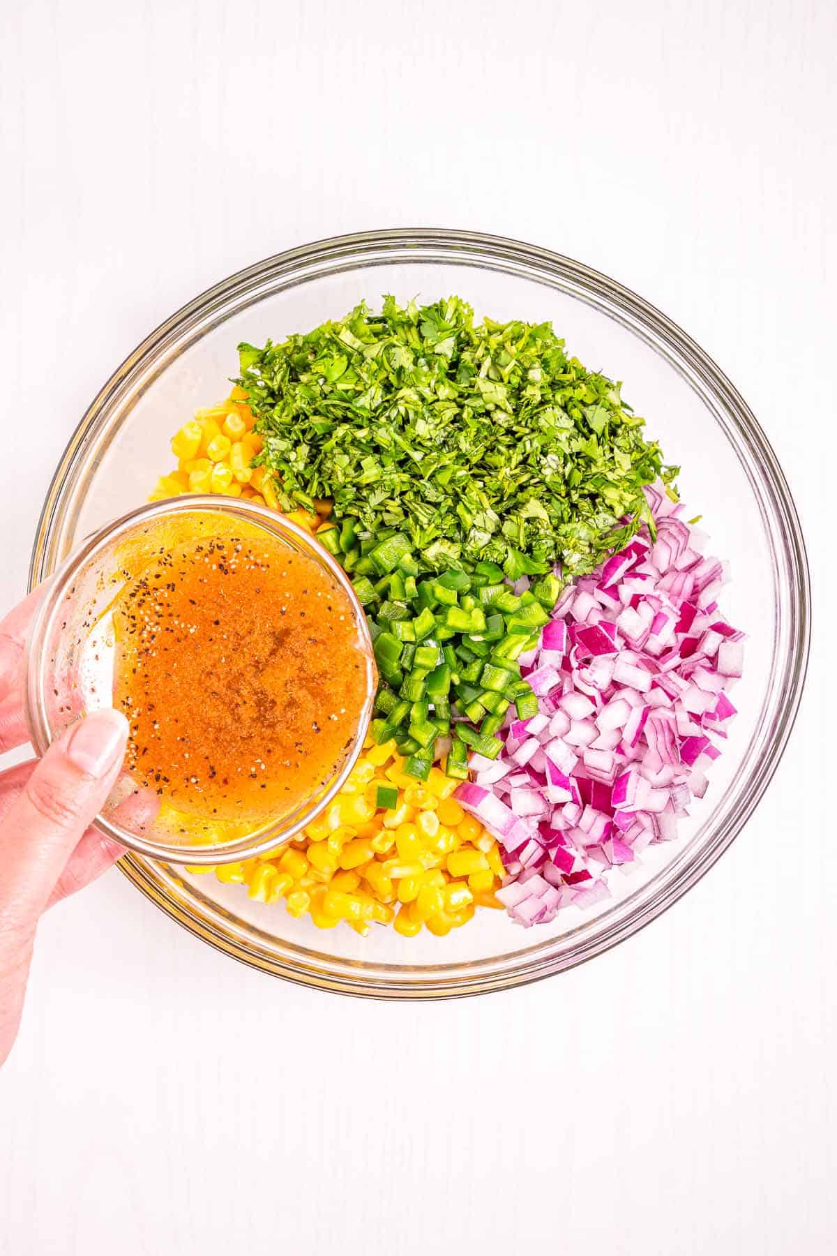Pouring lime dressing over corn salsa ingredients in a glass mixing bowl.