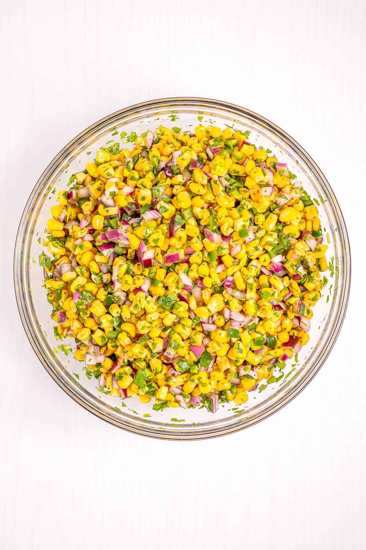 Fresh corn salsa mixed with red onion, cilantro, and lime juice in a glass bowl.