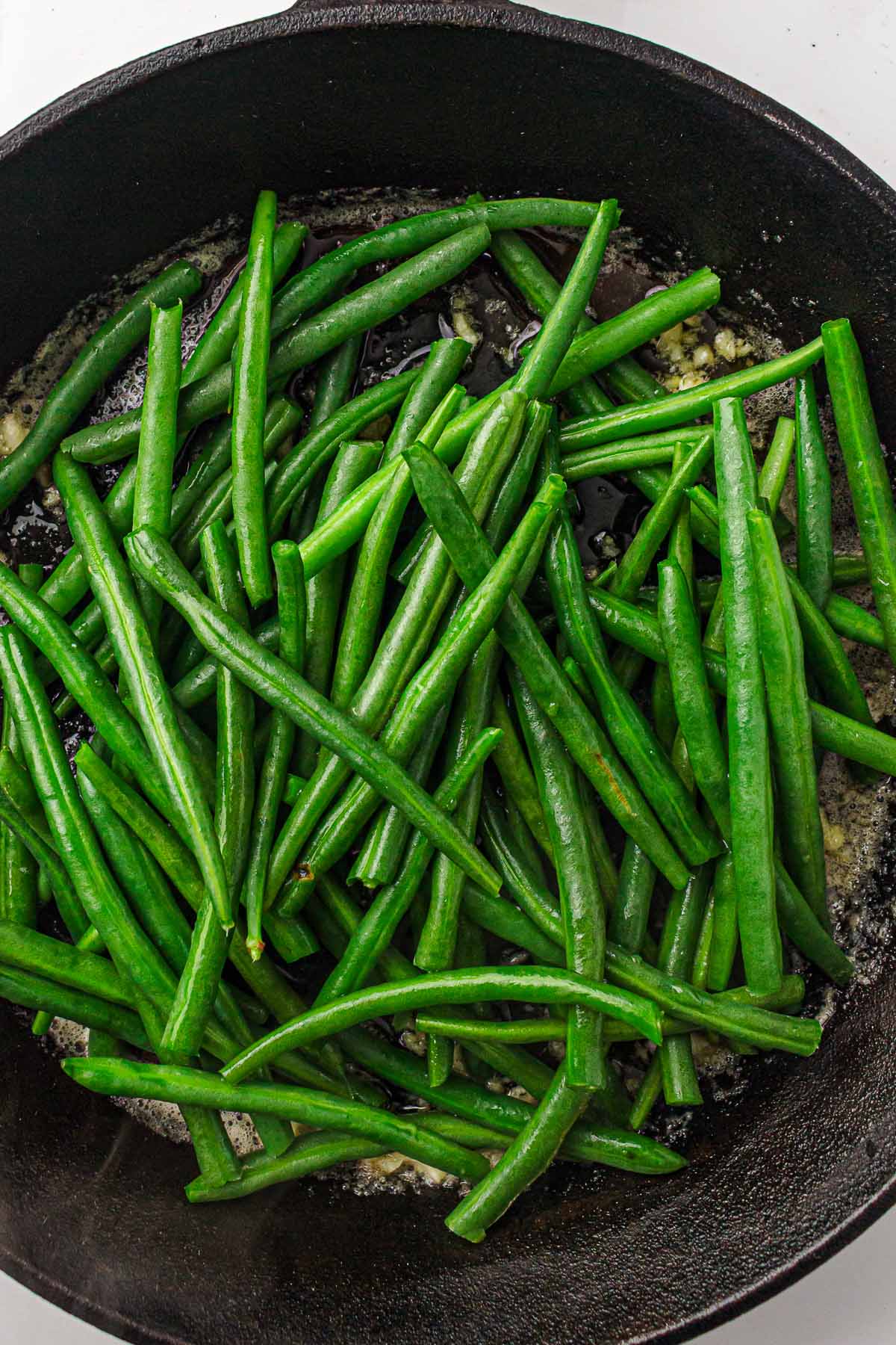 Cooked green beans evenly sautéed and glossy in a pan.