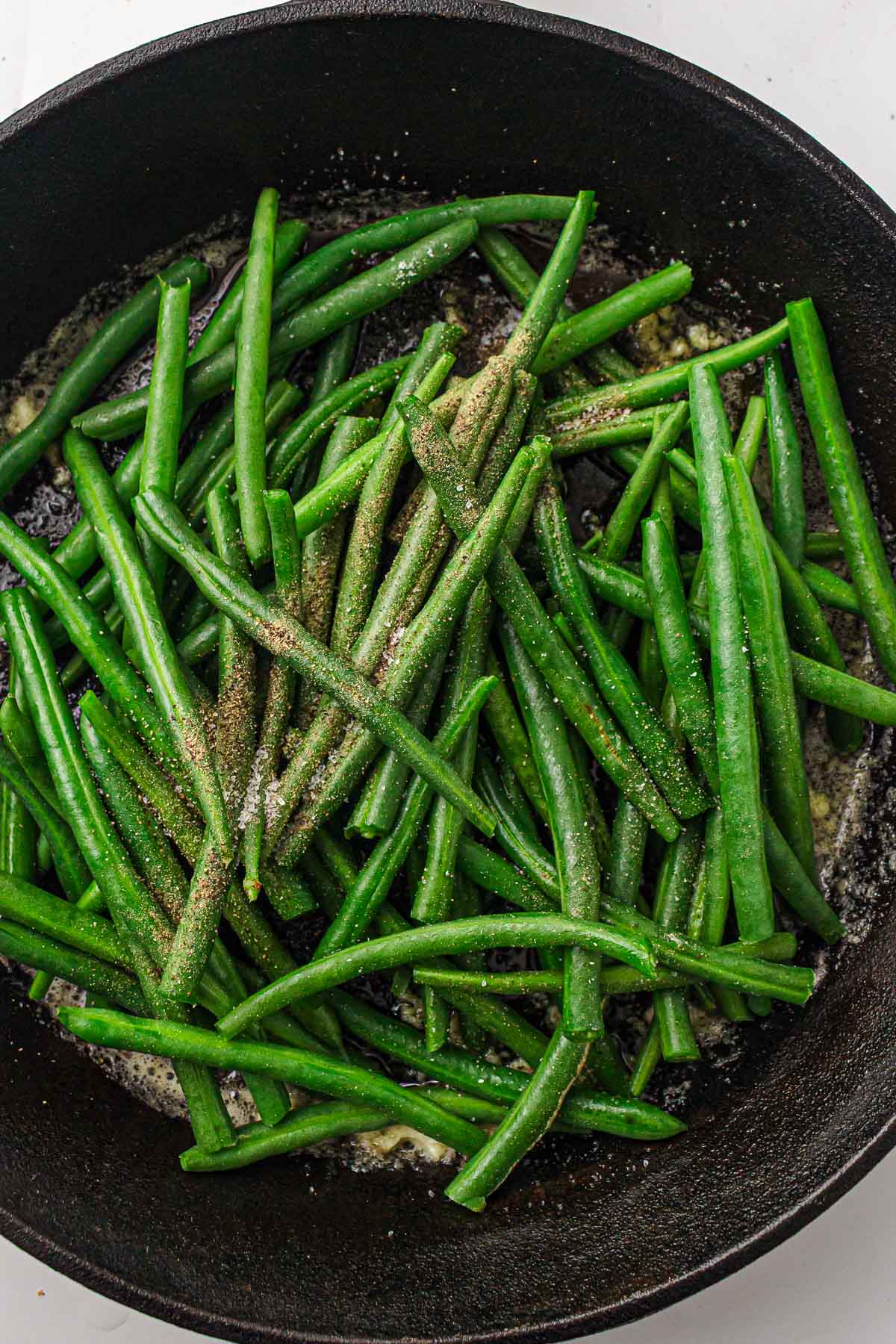 Green beans sautéing in a skillet with slight browning on some pieces.