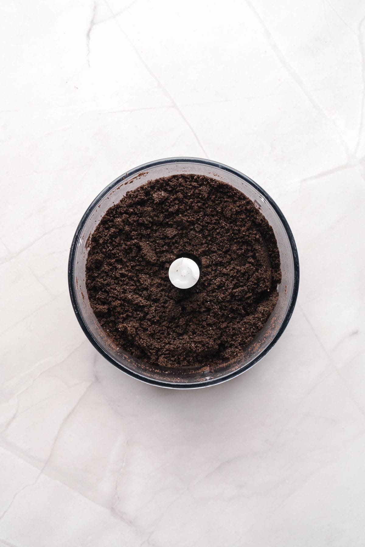 Crushed Oreo crumbs in a food processor bowl.