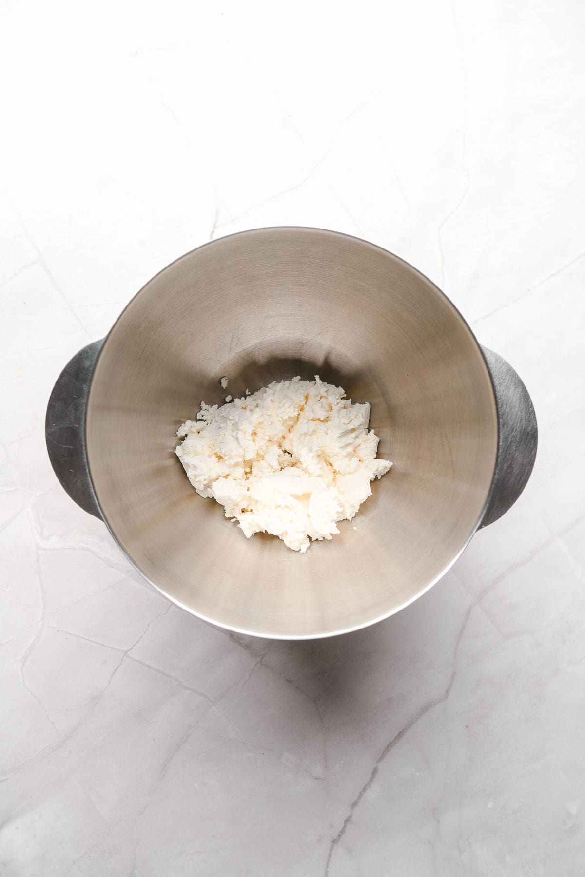 Softened cream cheese in a metal mixing bowl.