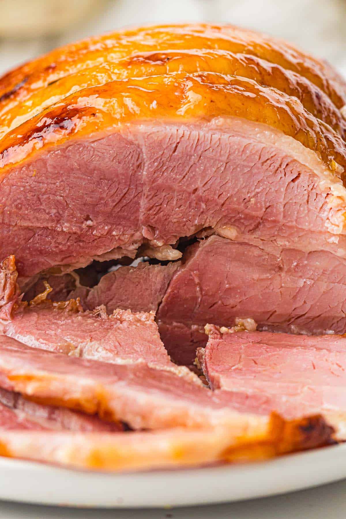 Half honey glazed ham with shiny glaze and several slices cut in front.