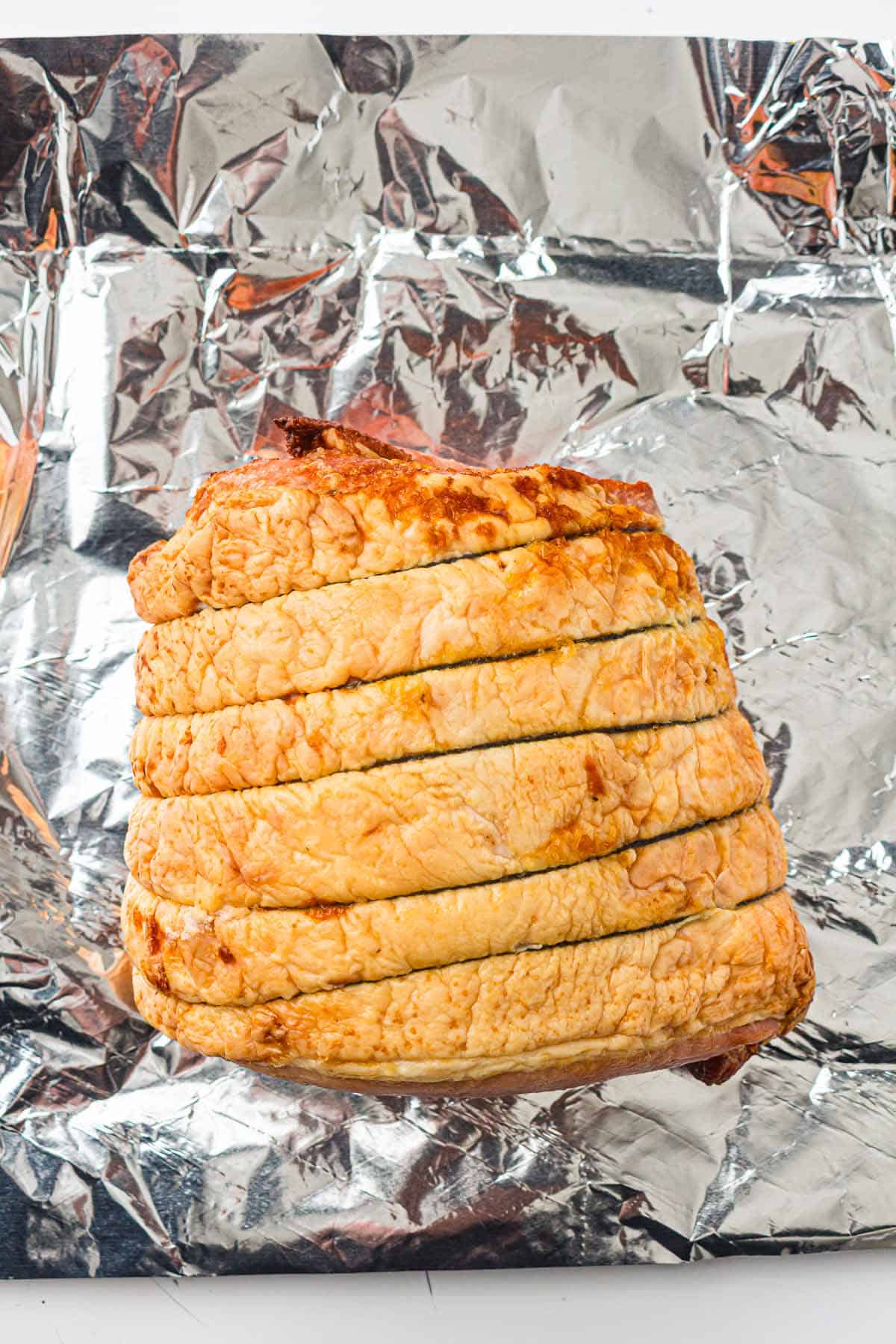 Scored ham joint resting on foil-lined surface.