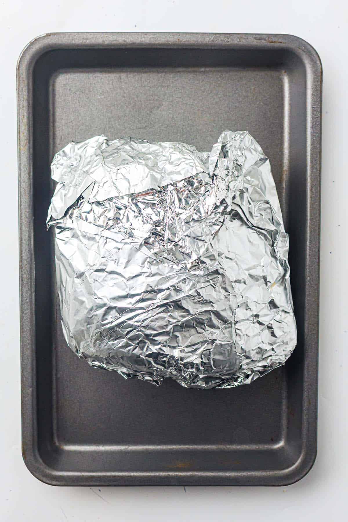 Ham wrapped in foil placed on a baking tray.