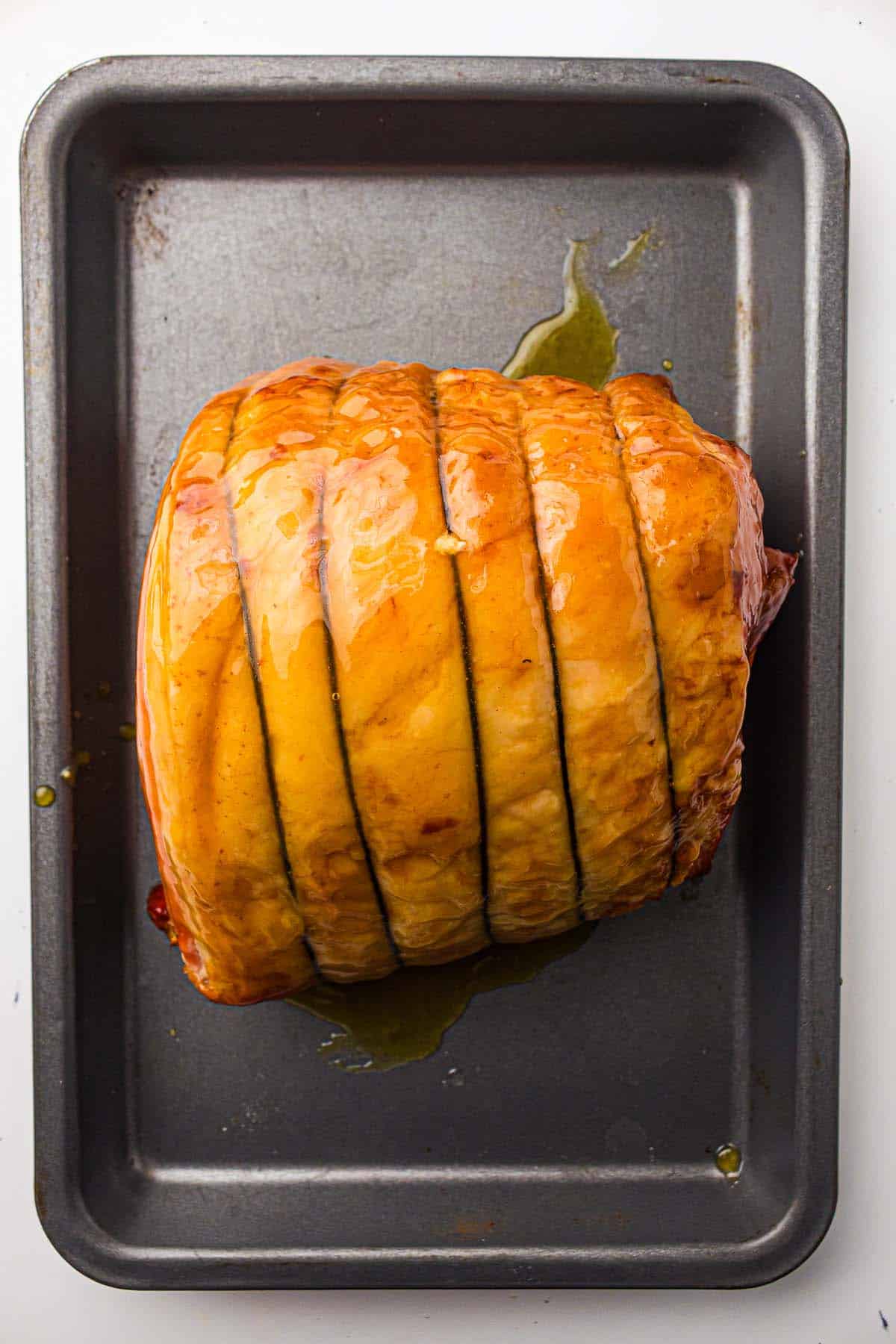 Ham joint roasting in a pan with glaze pooling underneath.