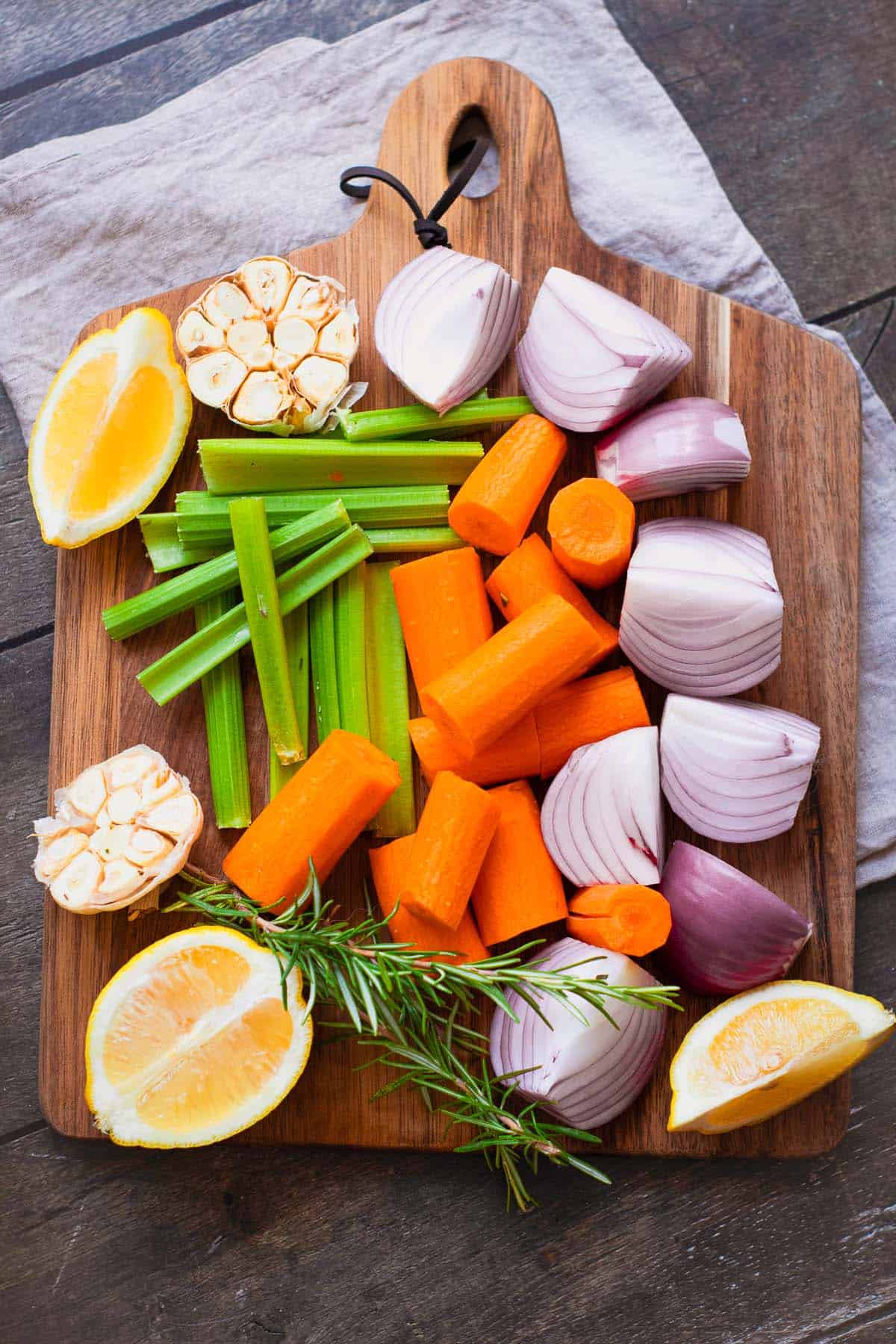Chopped carrots, celery, onion, garlic, lemon, and rosemary on a cutting board.