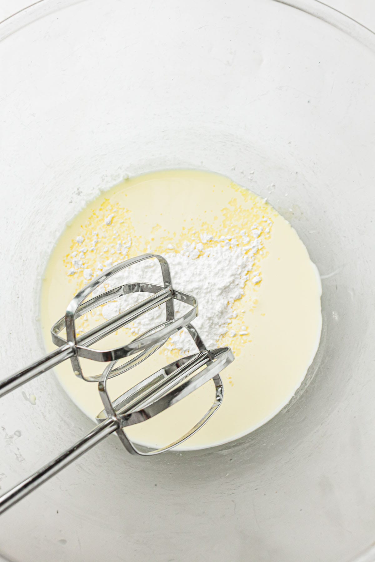Cream mixture being whipped with electric beaters in a bowl.