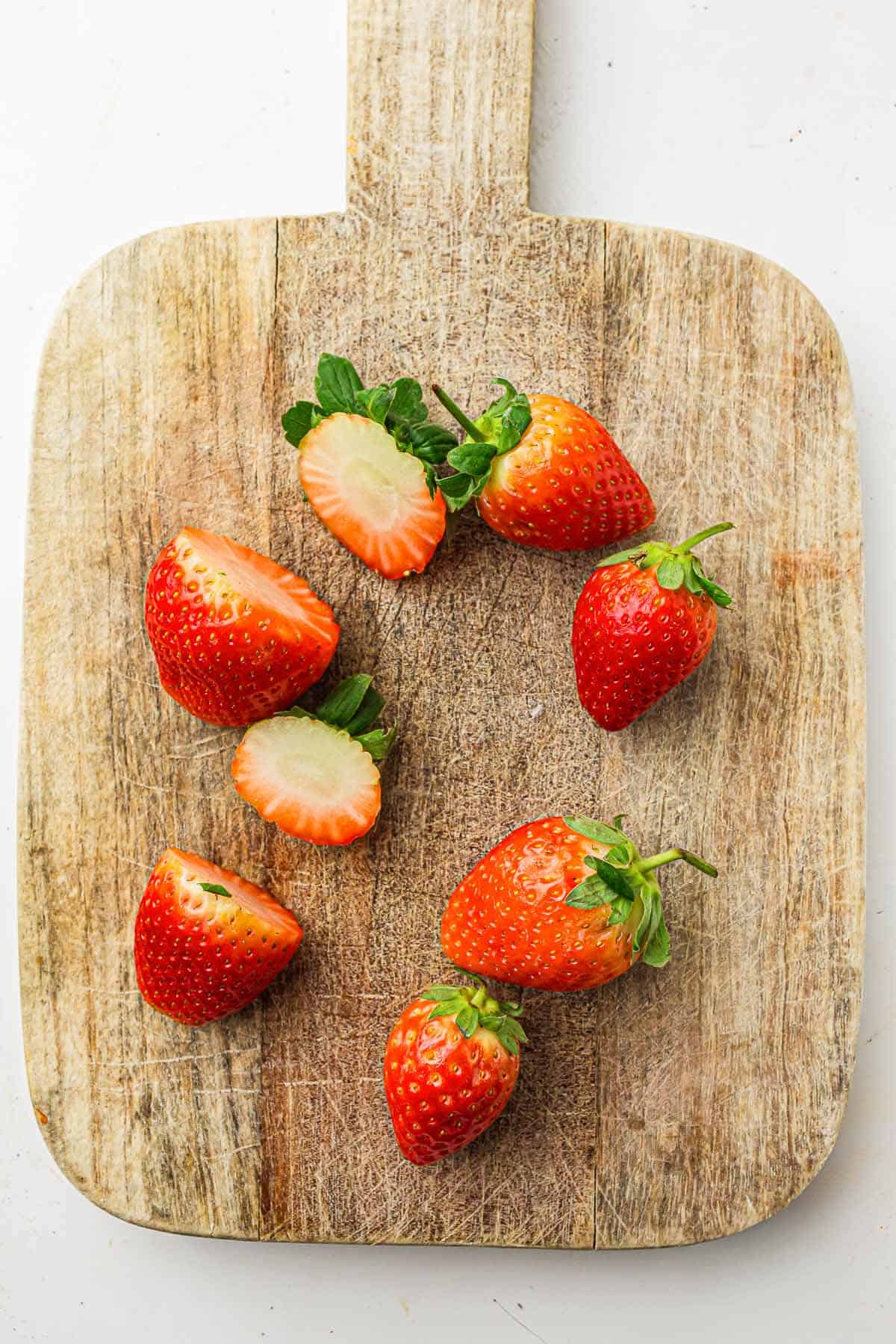 Whole and halved strawberries on a wooden cutting board.