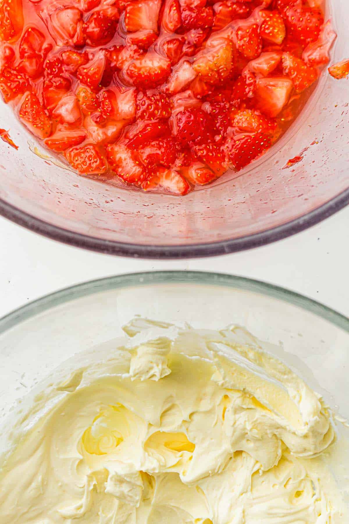 Chopped strawberries in syrup above whipped cream in a bowl.