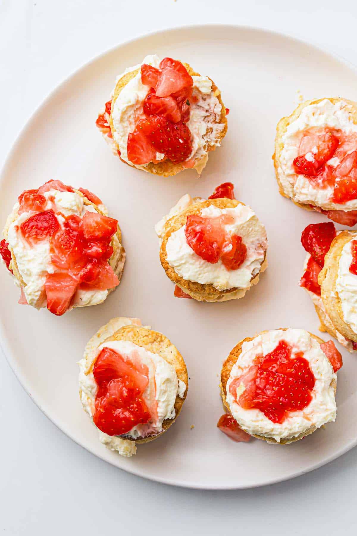 Mini strawberry shortcakes assembled on a plate with cream and fruit.