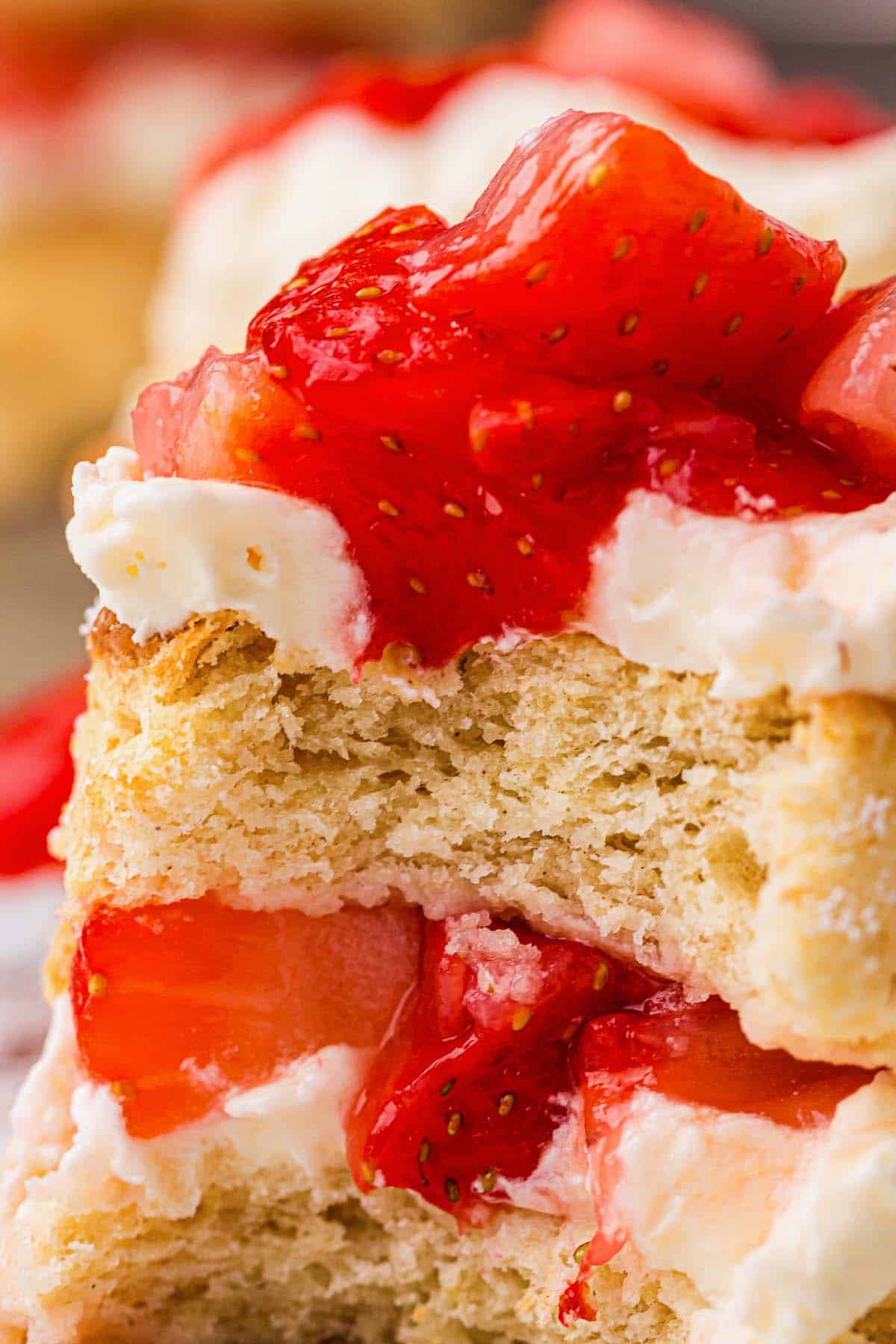 Close-up of strawberry shortcake layers with whipped cream and glossy strawberry topping.