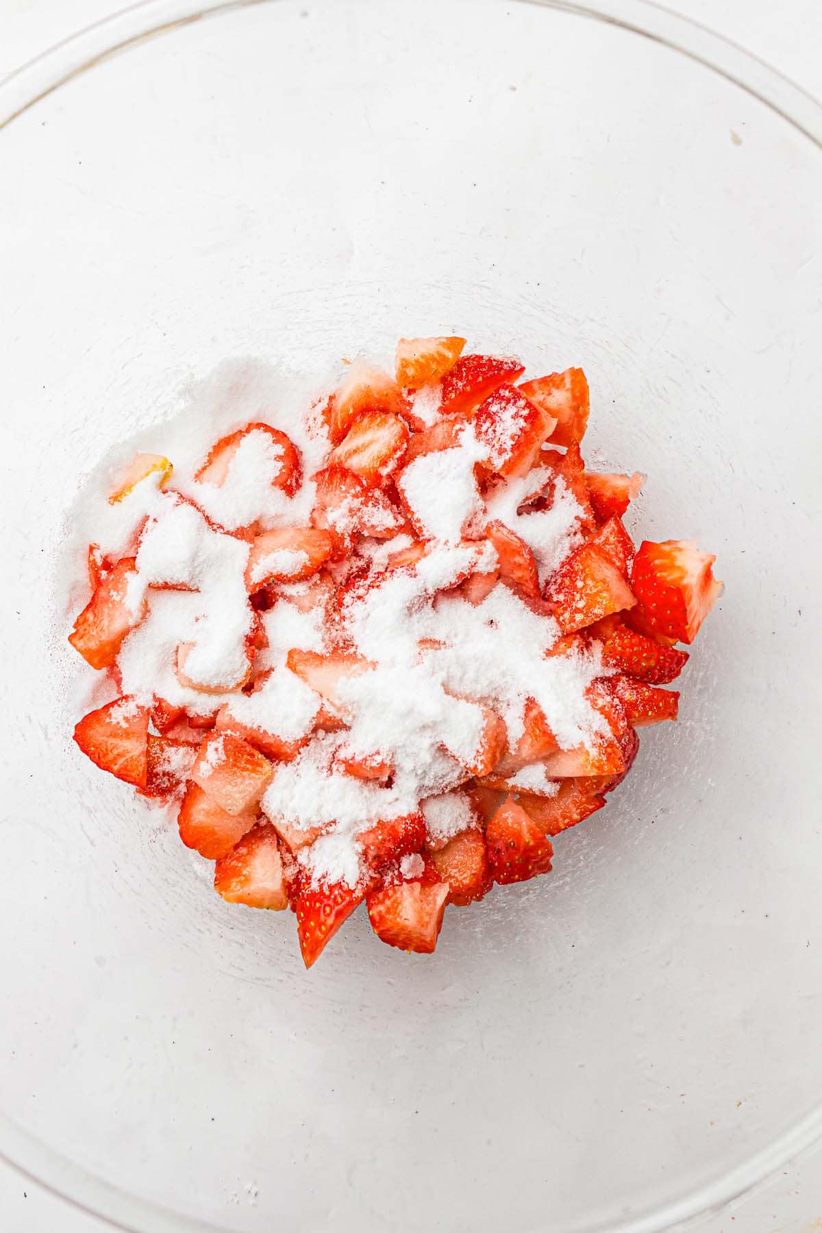 Chopped strawberries sprinkled with sugar in a glass bowl.