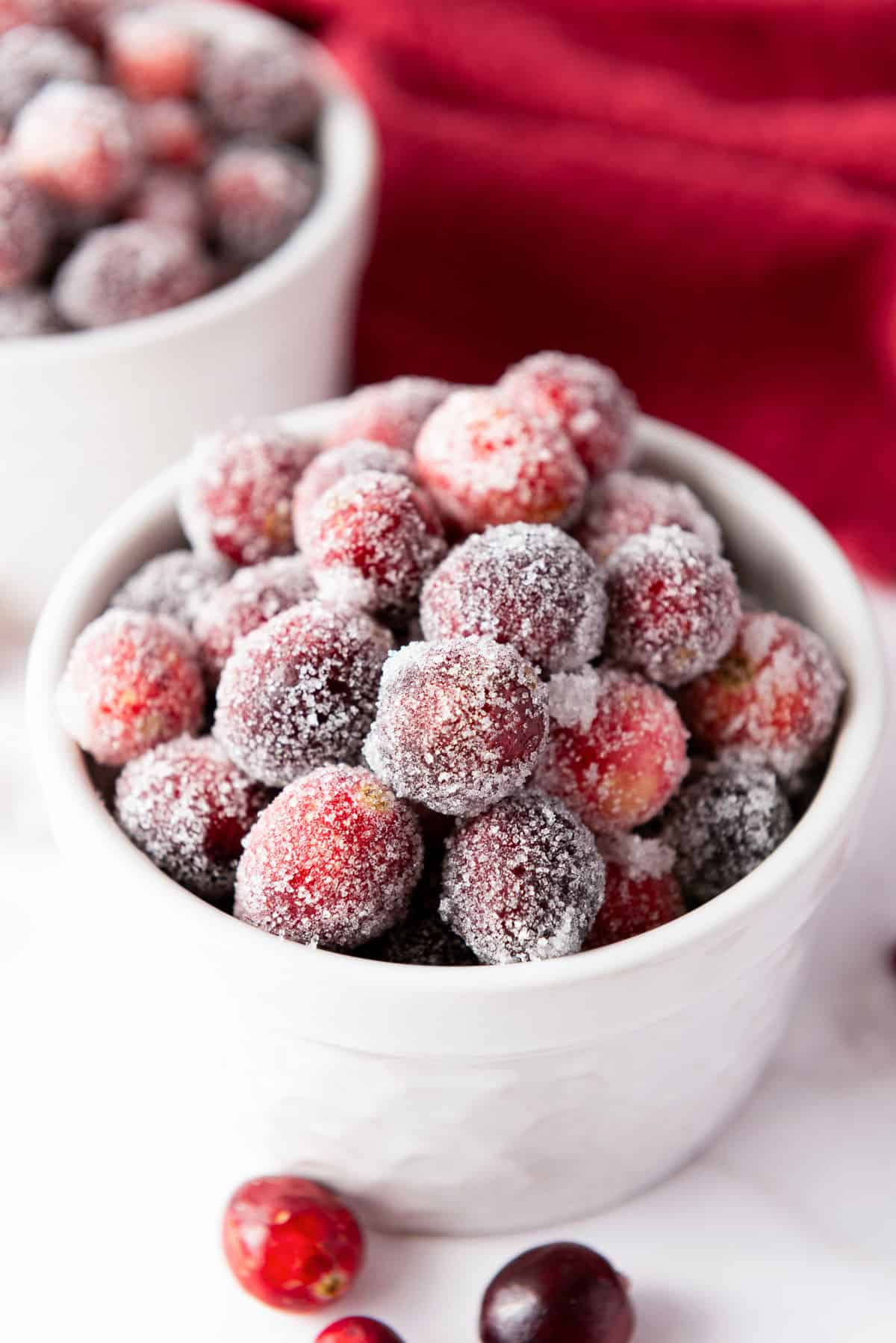 White bowls filled with sugared cranberries, coated in sparkling sugar, on a white surface.