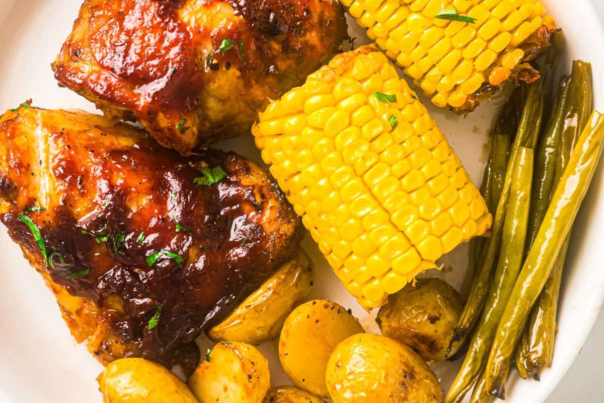 Roasted chicken with corn, green beans, and baby potatoes on a plate.