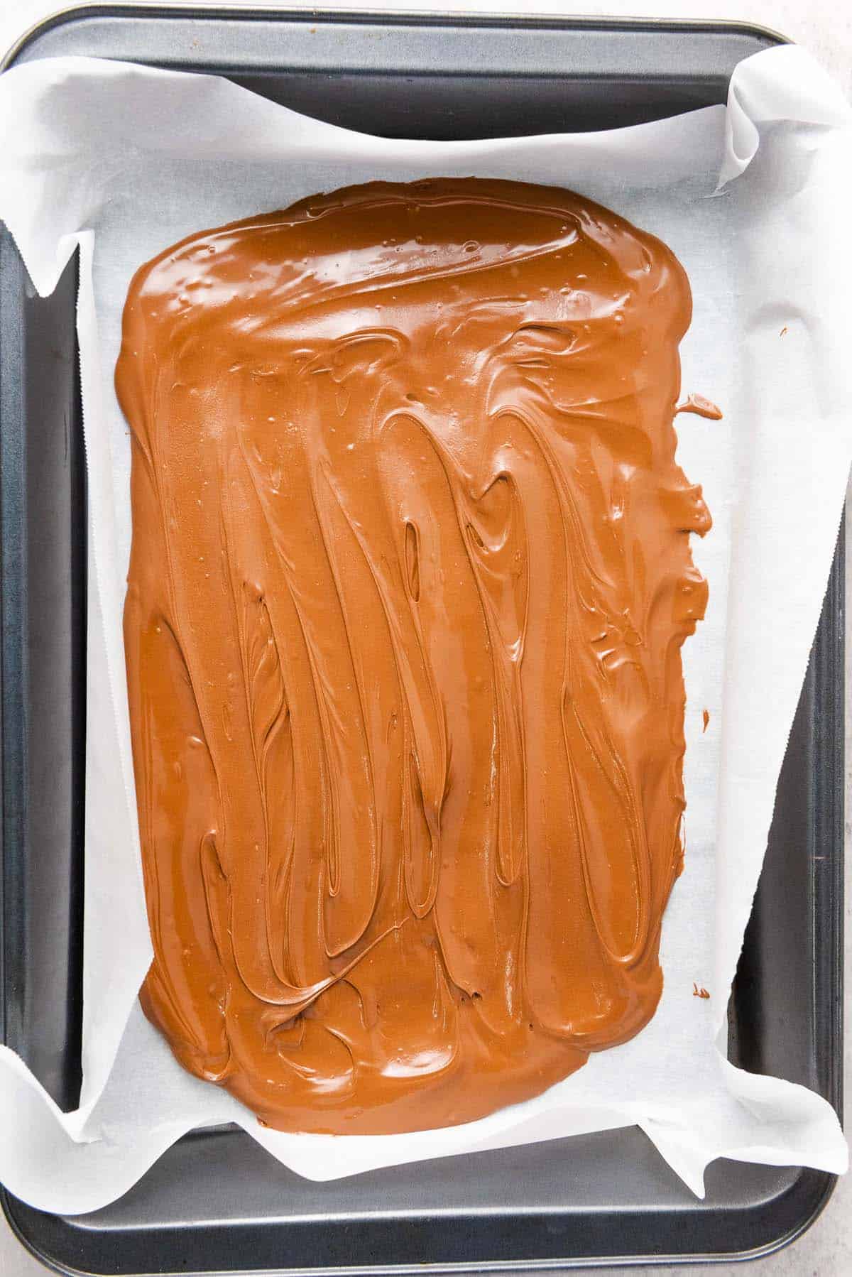 Melted chocolate spread on parchment-lined baking pan.