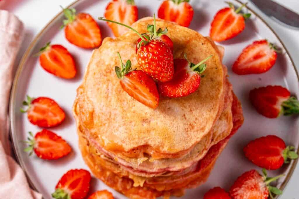 Strawberry pancakes topped with fresh strawberries on a white plate