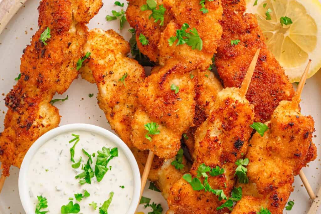 Breaded chicken skewers with dipping sauce on a plate