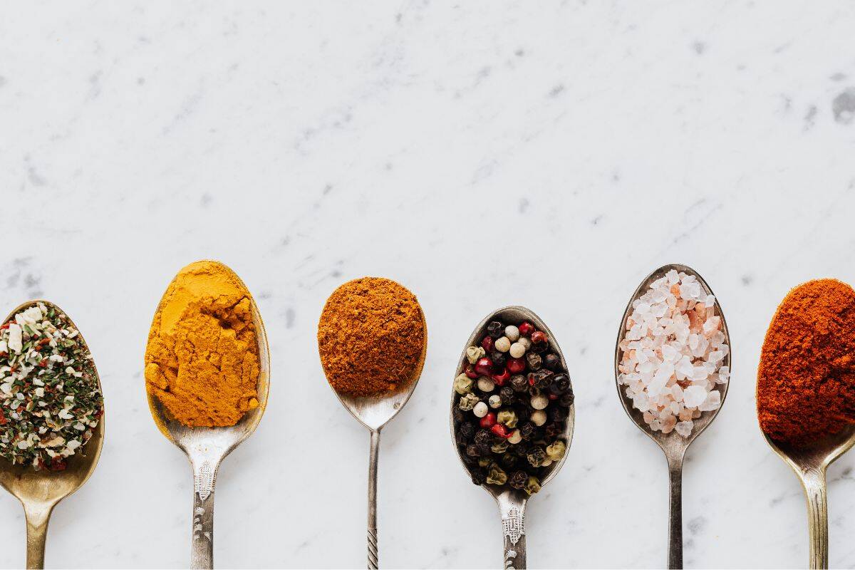 Spoons with colorful spices like turmeric, pepper, and salt on white surface