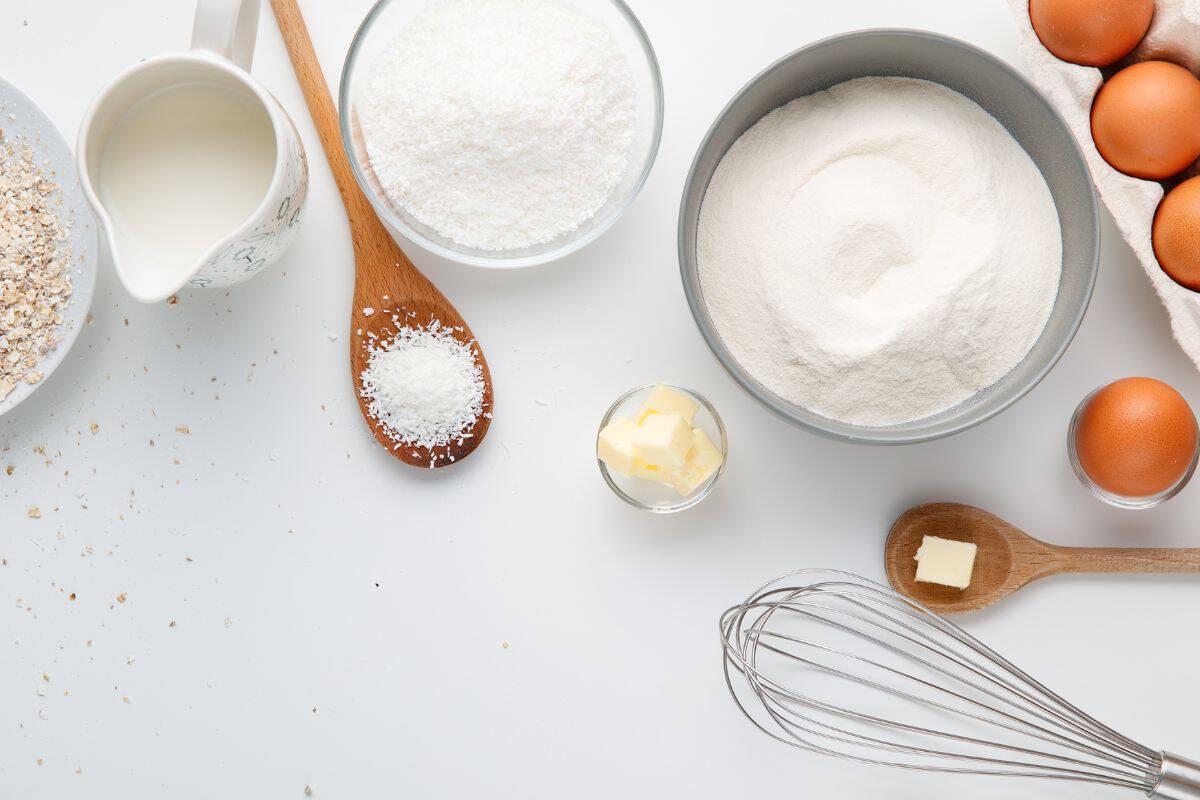 Baking ingredients like flour, eggs, butter, and whisk on white background