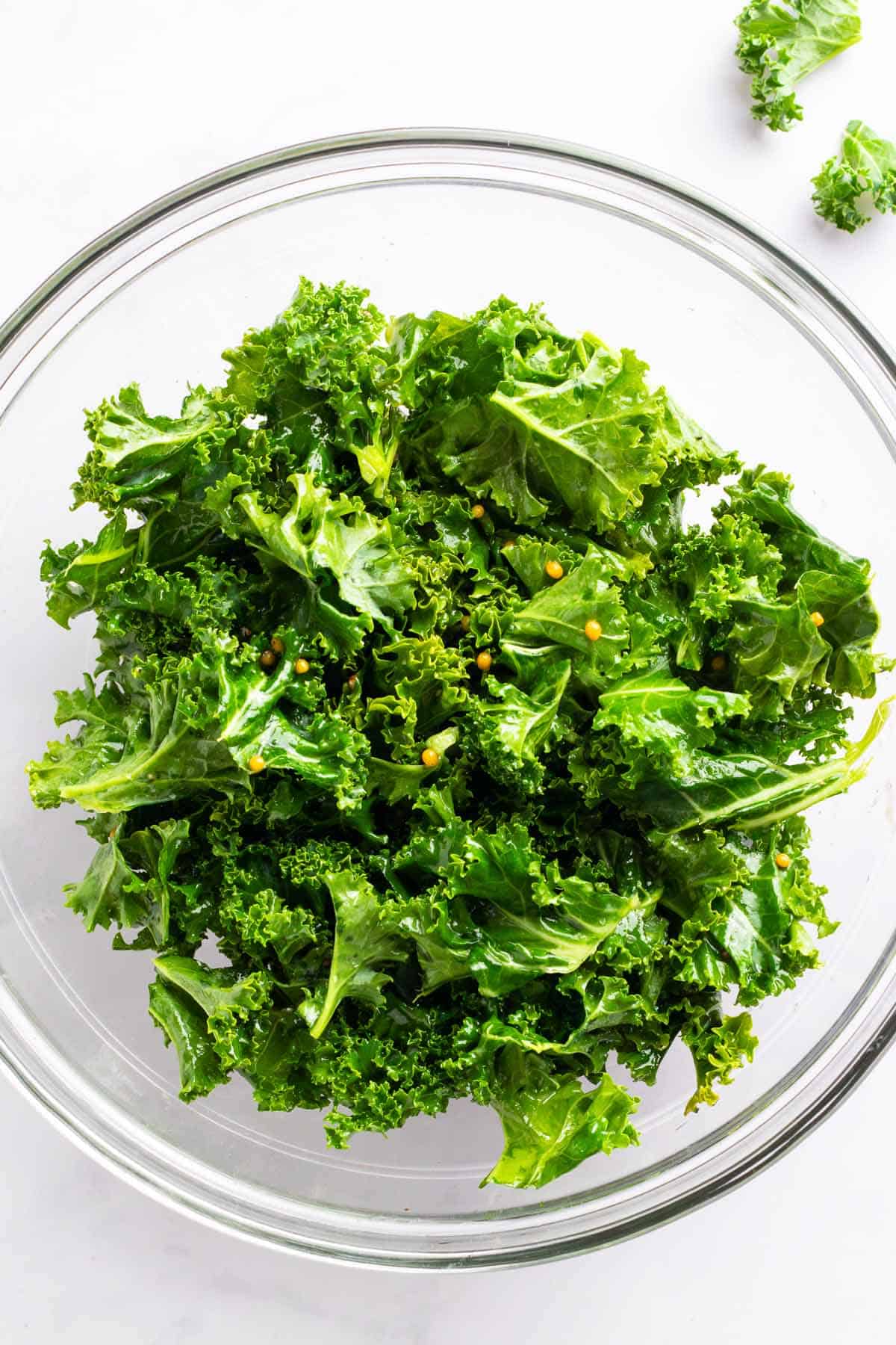 Massaged kale leaves coated with dressing in a glass mixing bowl