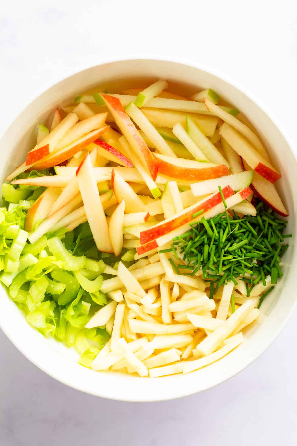 Sliced apples, parsnip, celery, and chives prepared for kale salad