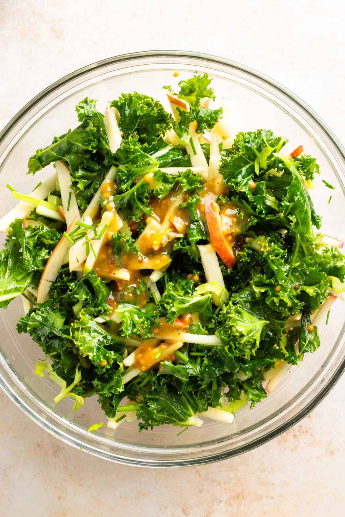 Kale salad tossed with apples and miso dressing in a glass bowl