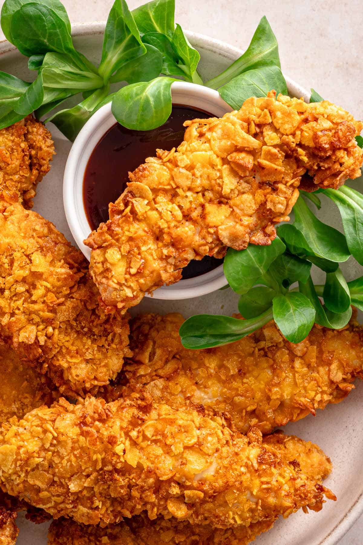 Crispy cornflake chicken tenders served with barbecue dipping sauce and fresh greens