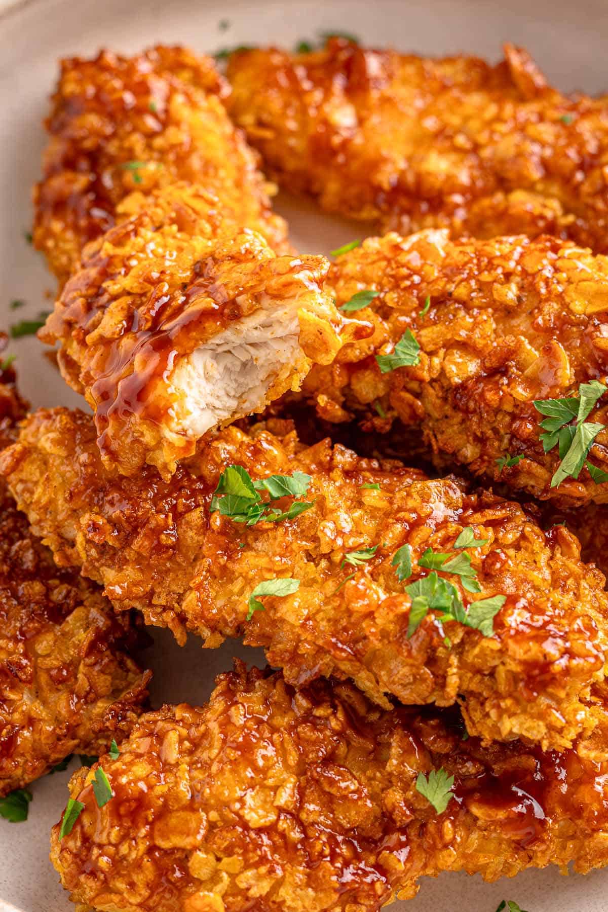 Cornflake chicken tenders drizzled with barbecue sauce, one piece cut open