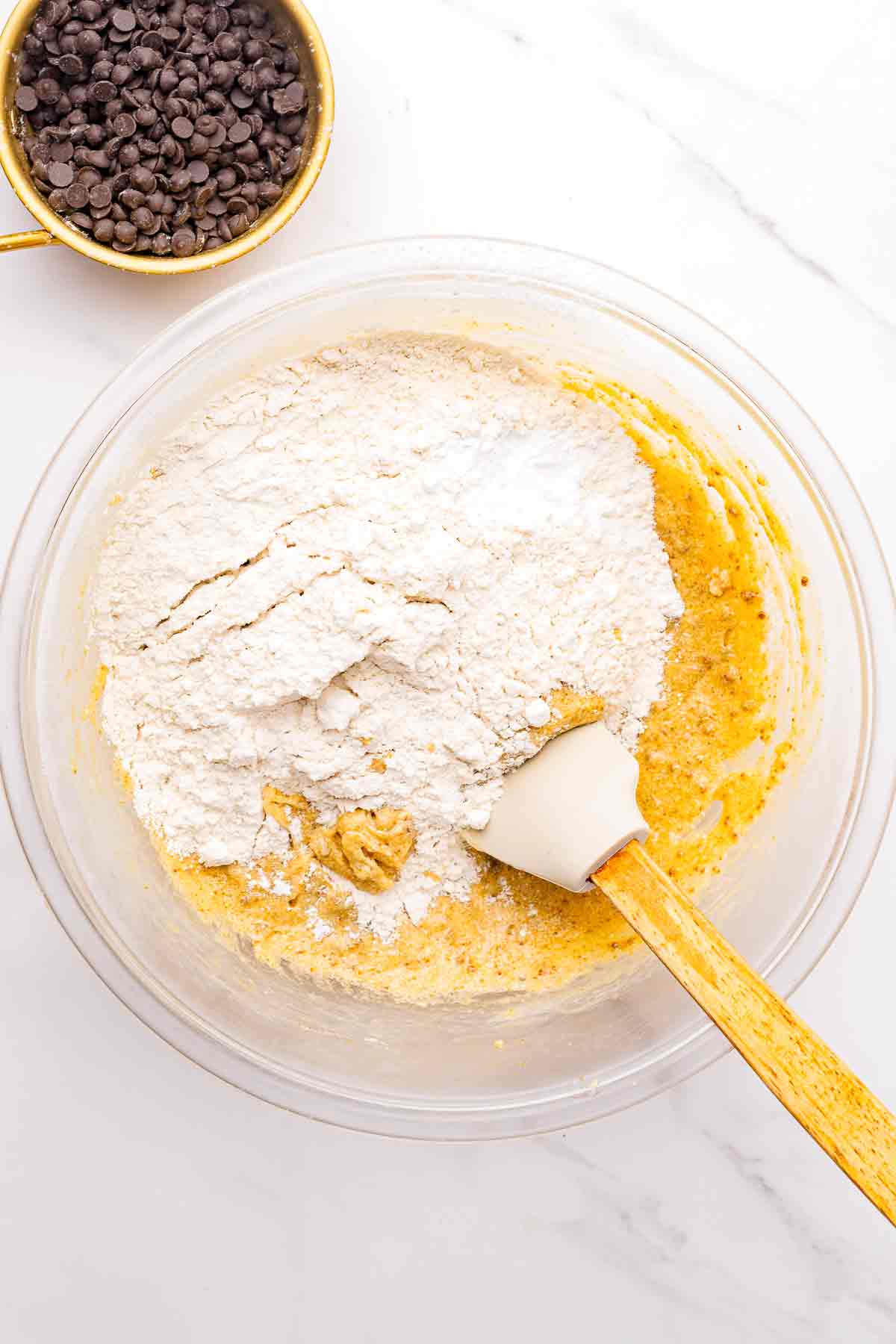 Flour added to cookie dough mixture in a glass mixing bowl