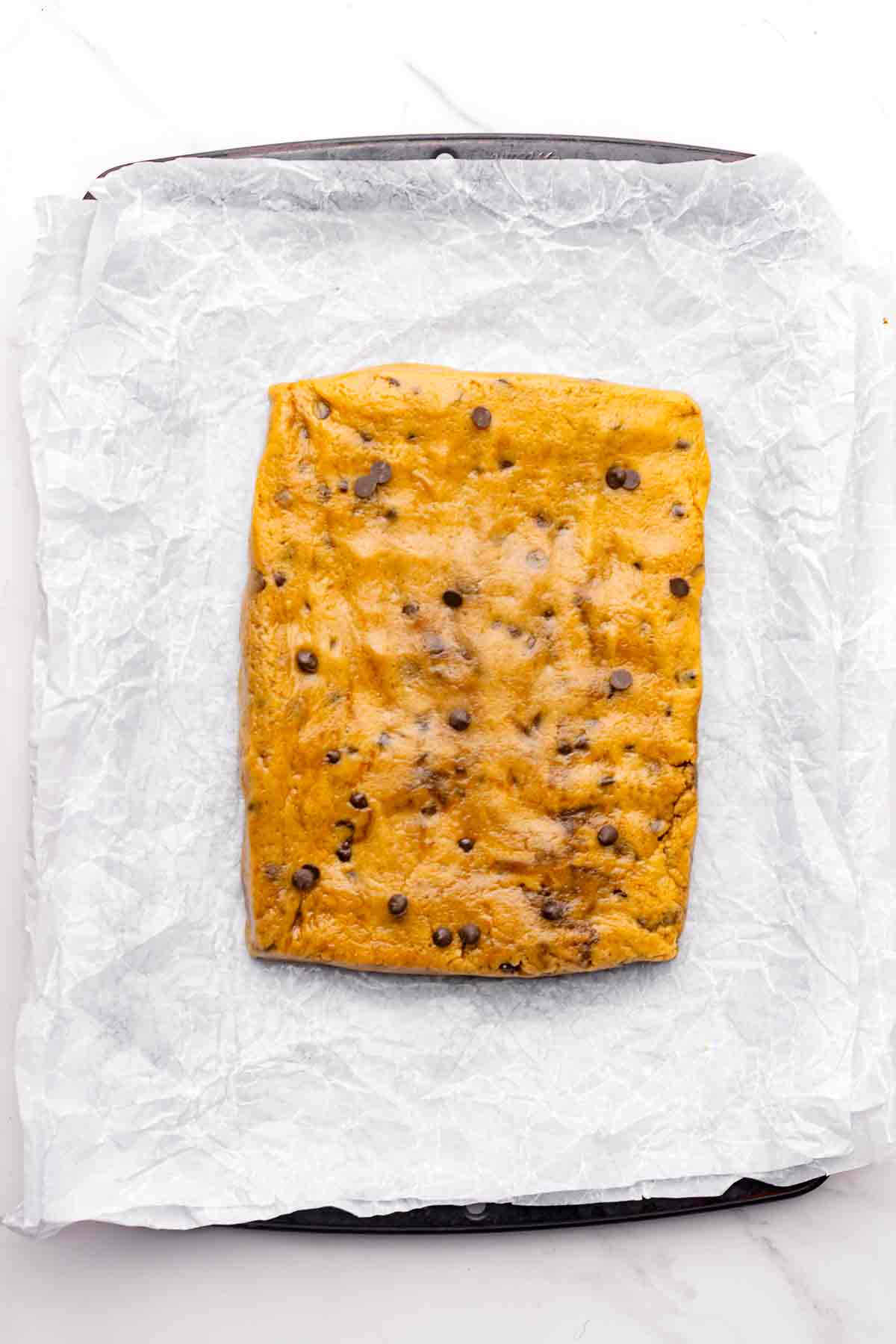 Flattened chocolate chip cookie dough on parchment-lined baking sheet