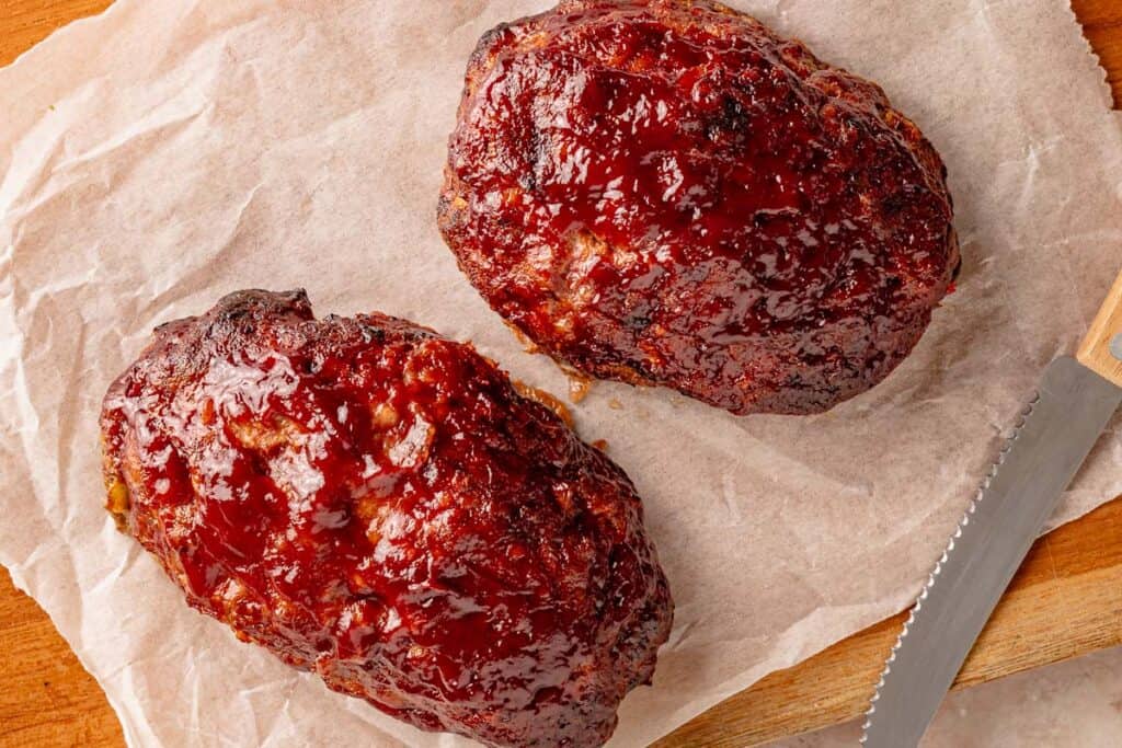 Two glazed meatloaves on parchment paper beside a knife