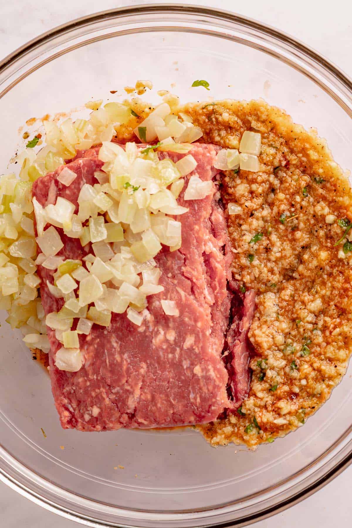 Ground beef, onion, and seasonings in a glass mixing bowl