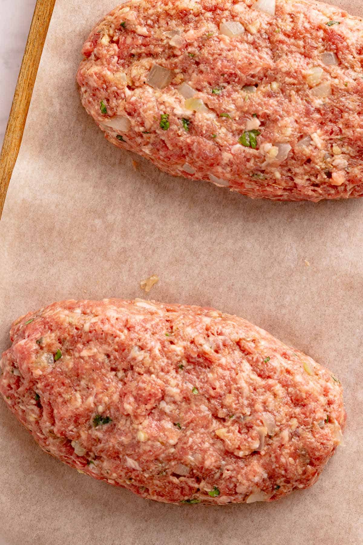 Two raw meatloaves shaped on parchment paper