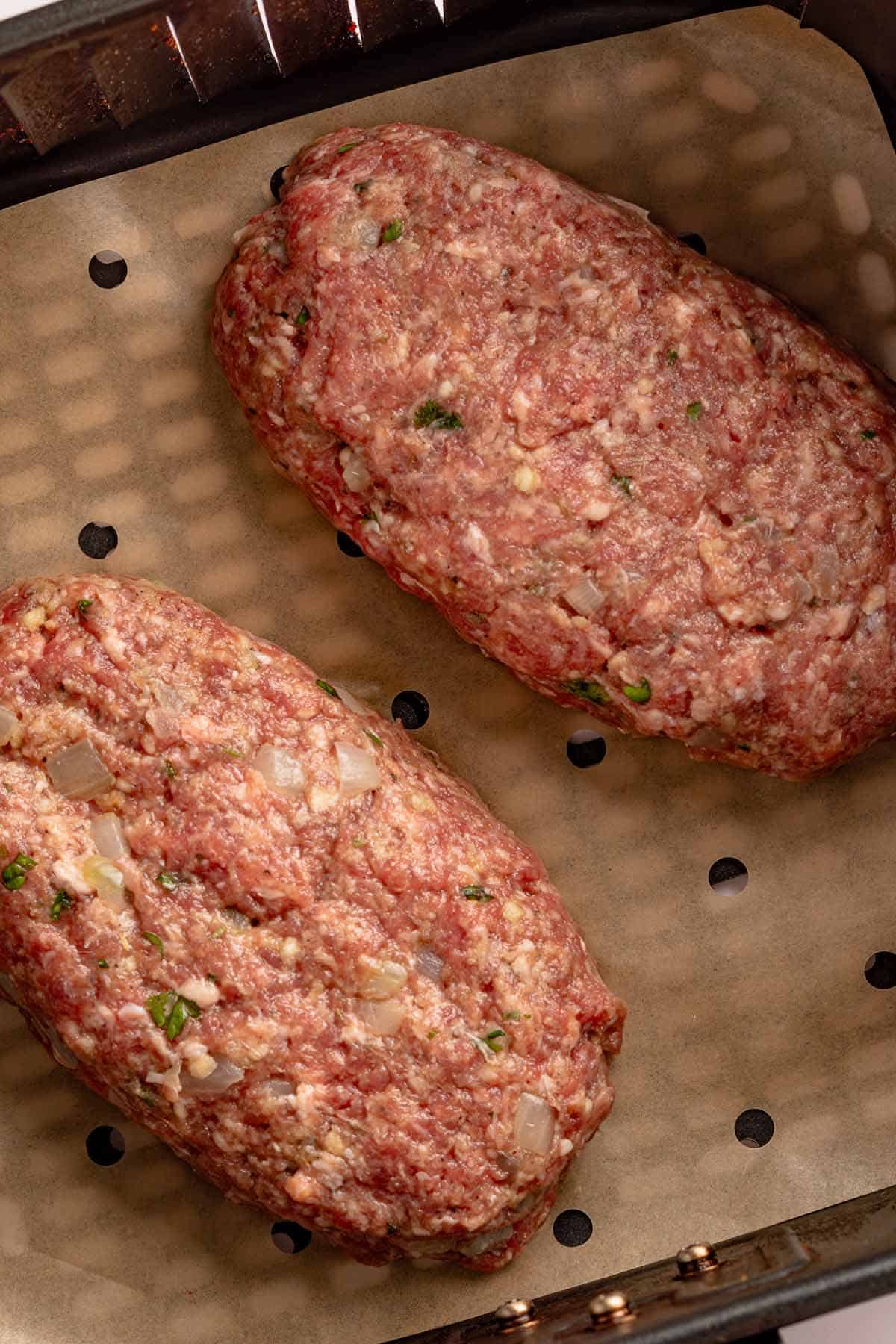 Two raw meatloaves in a parchment-lined air fryer basket